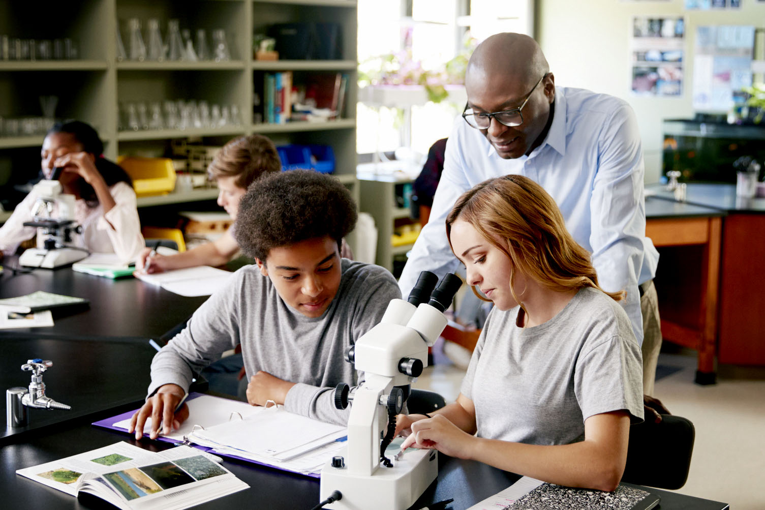 Teacher standing with two students as they work with a microscope