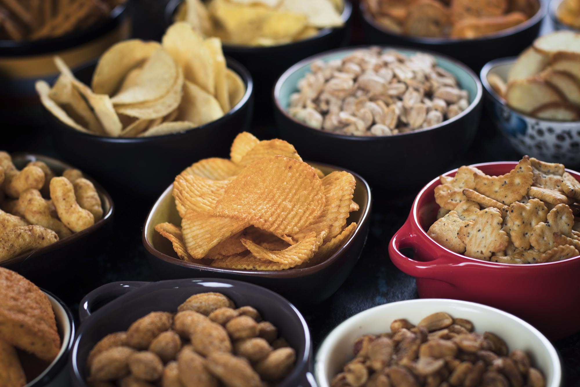 Various shaped bowls filled with various snacks including chips, nuts, crackers