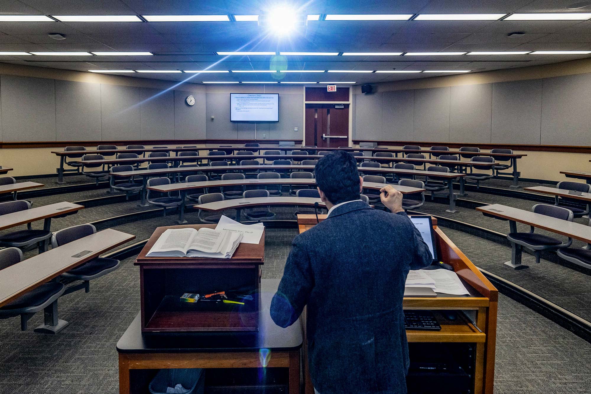 Professor standing at a podium with an empty classroom while on zoom