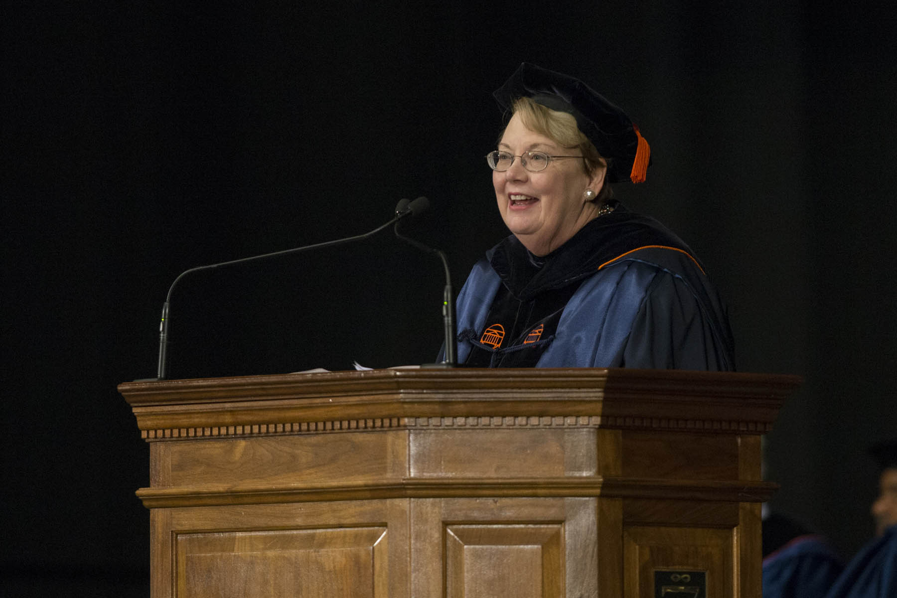 President Teresa Sullivan standing at a podium giving a speech in  a graduation gown