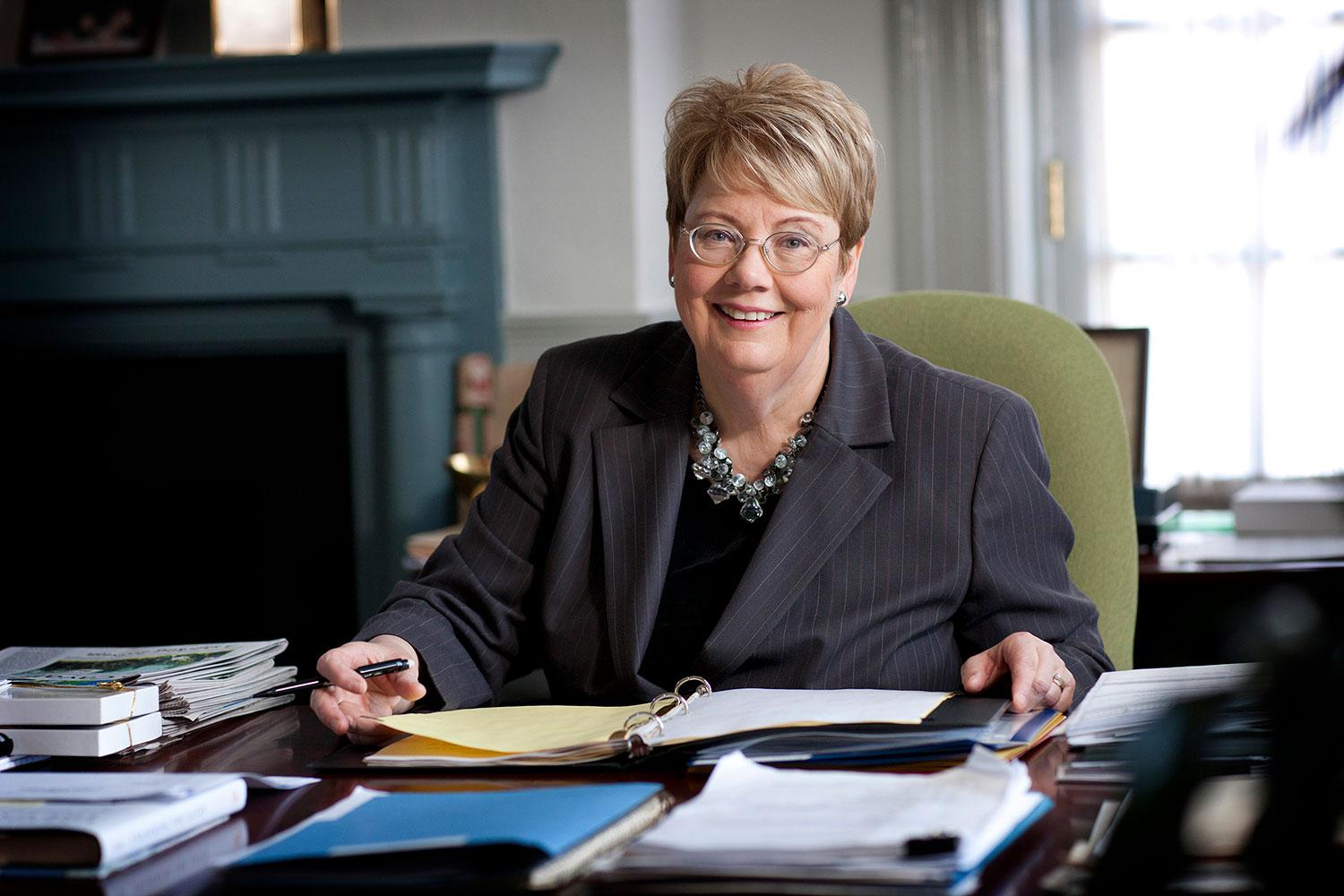 President Teresa A. Sullivan working at her desk smiling at the camera