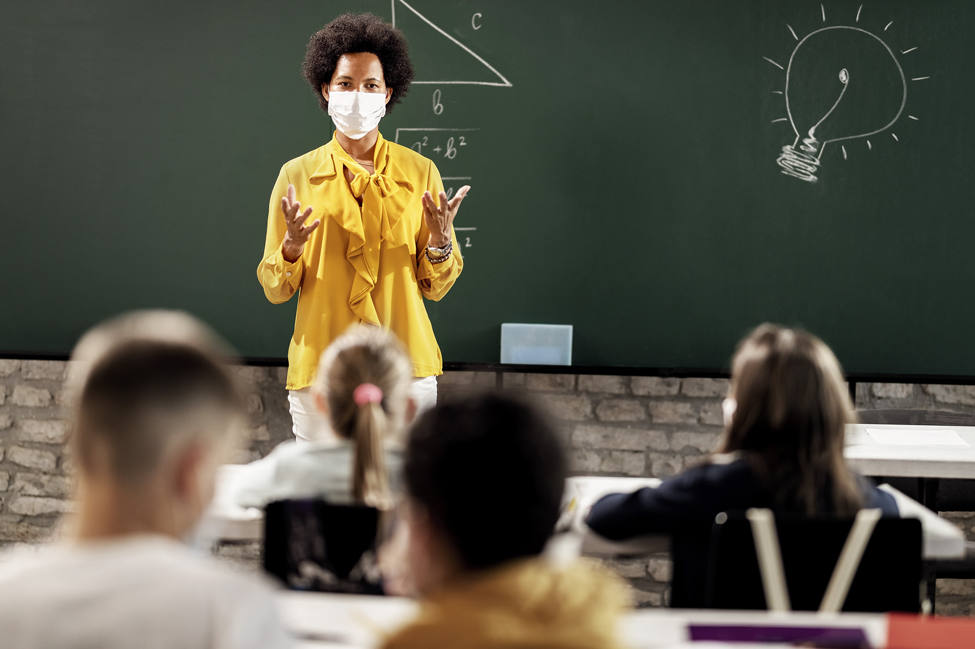 Professor teaching at the front of the class while the students are socially distanced