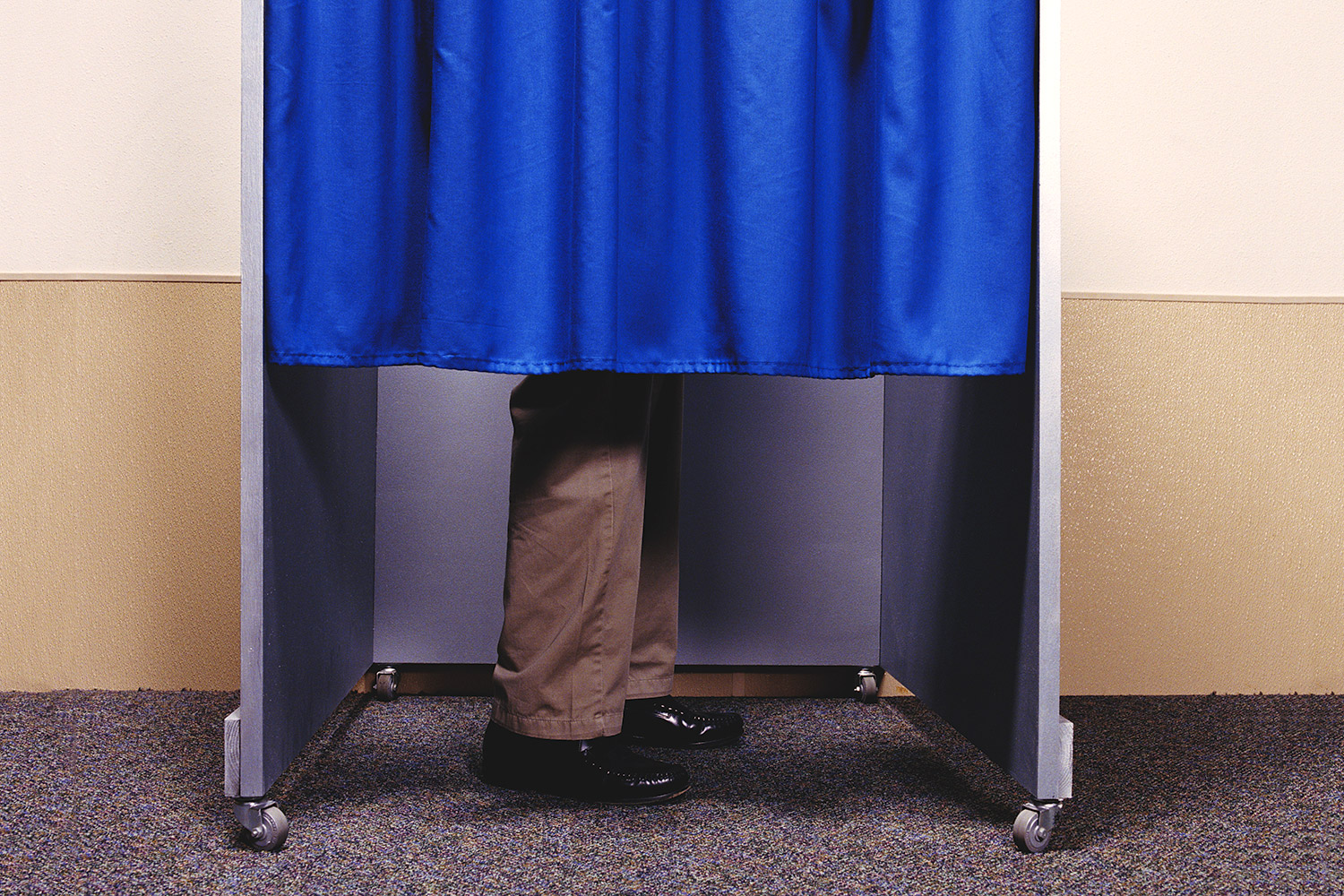 Person in a voting booth with a blue curtain pulled