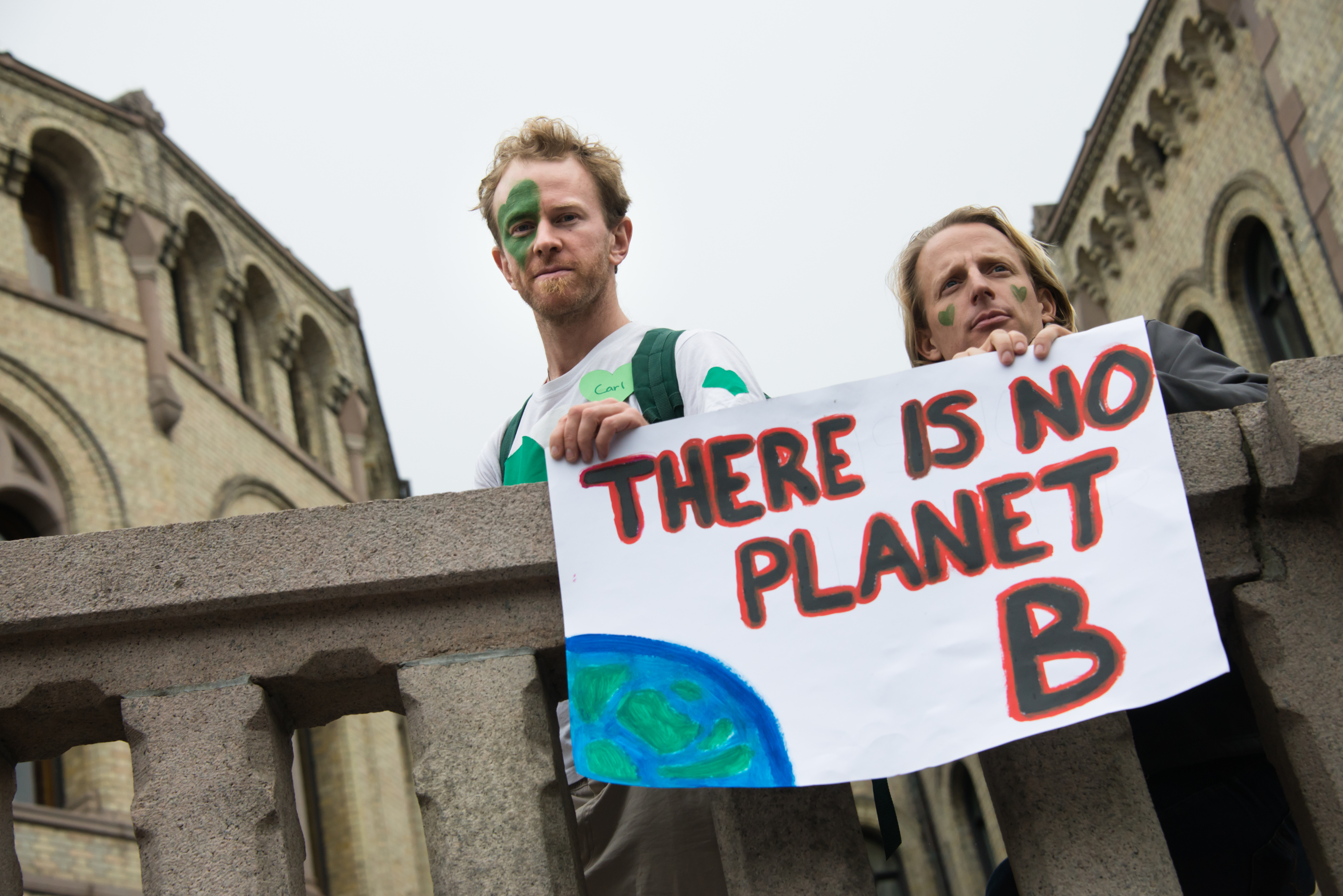 Two protestors in Norway hold a sign over a bridge that reads There is no planet B