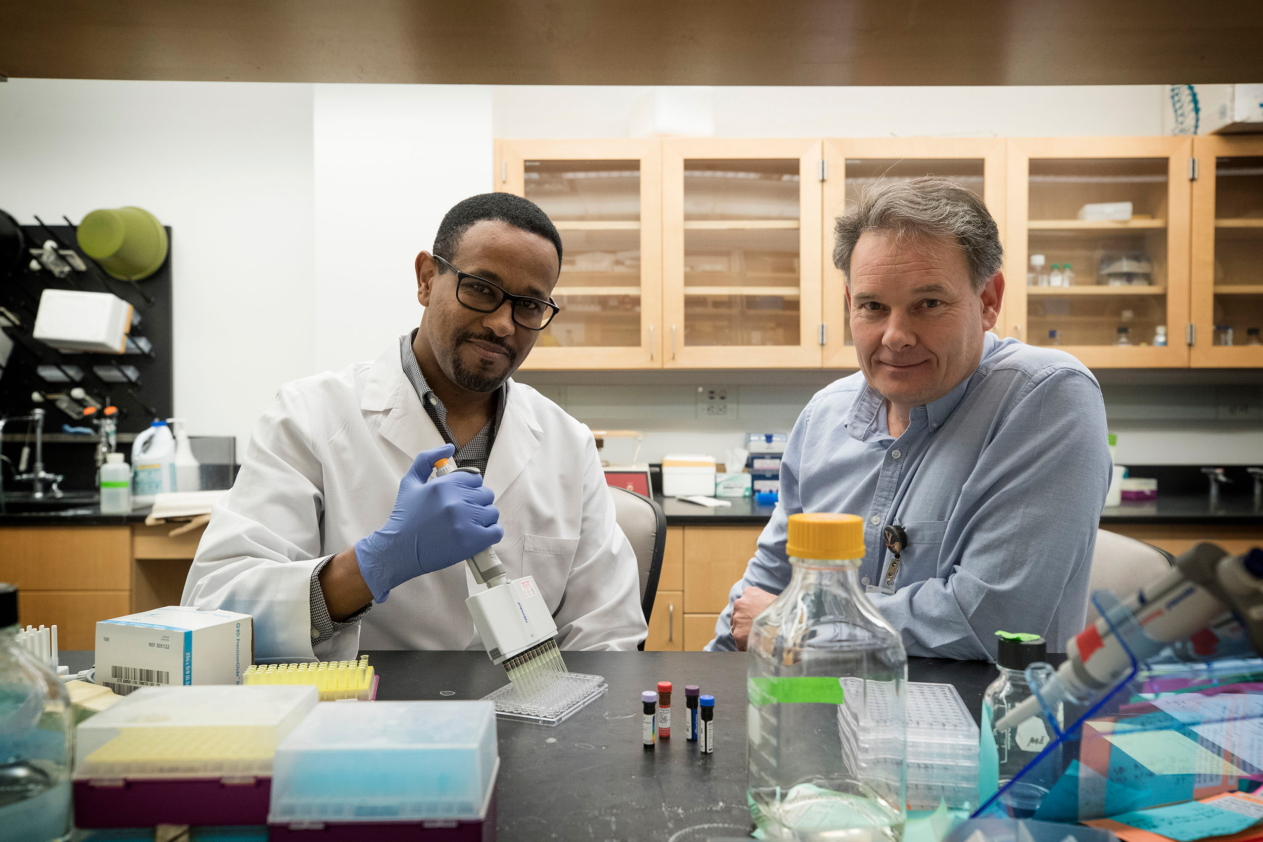 Medical researchers Lelisa Gemta, left, and Timothy Bullock working on an experiment together in the lab look at the camera
