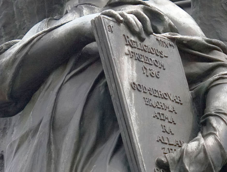 A statue of Thomas Jefferson holding a tablet with the names of different belief systems