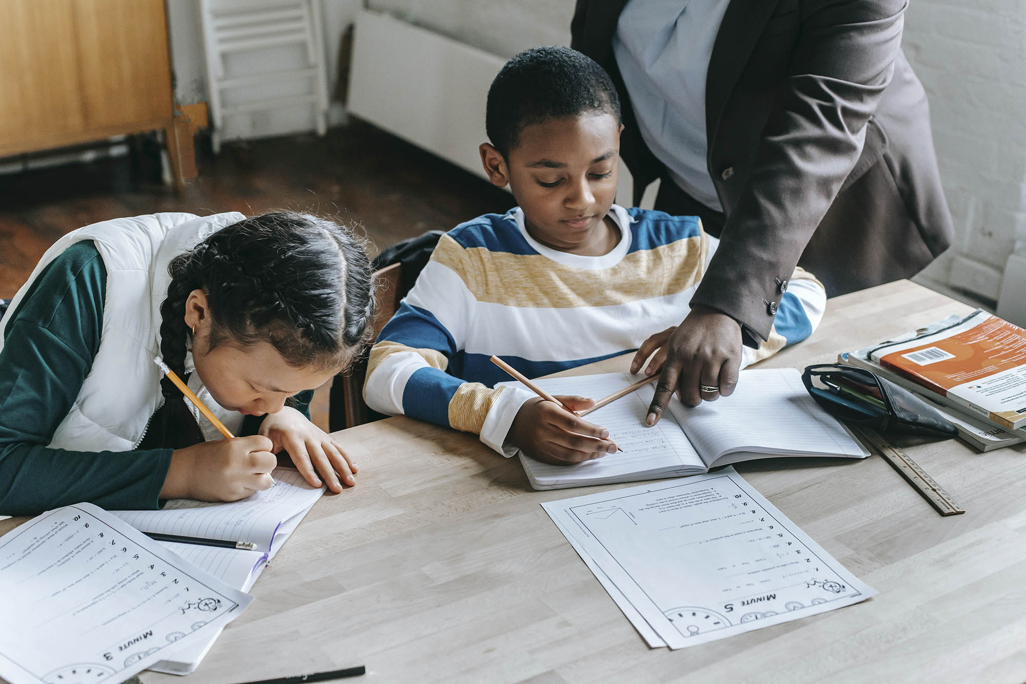 Children working on homework at dinner table with an Adult helping them