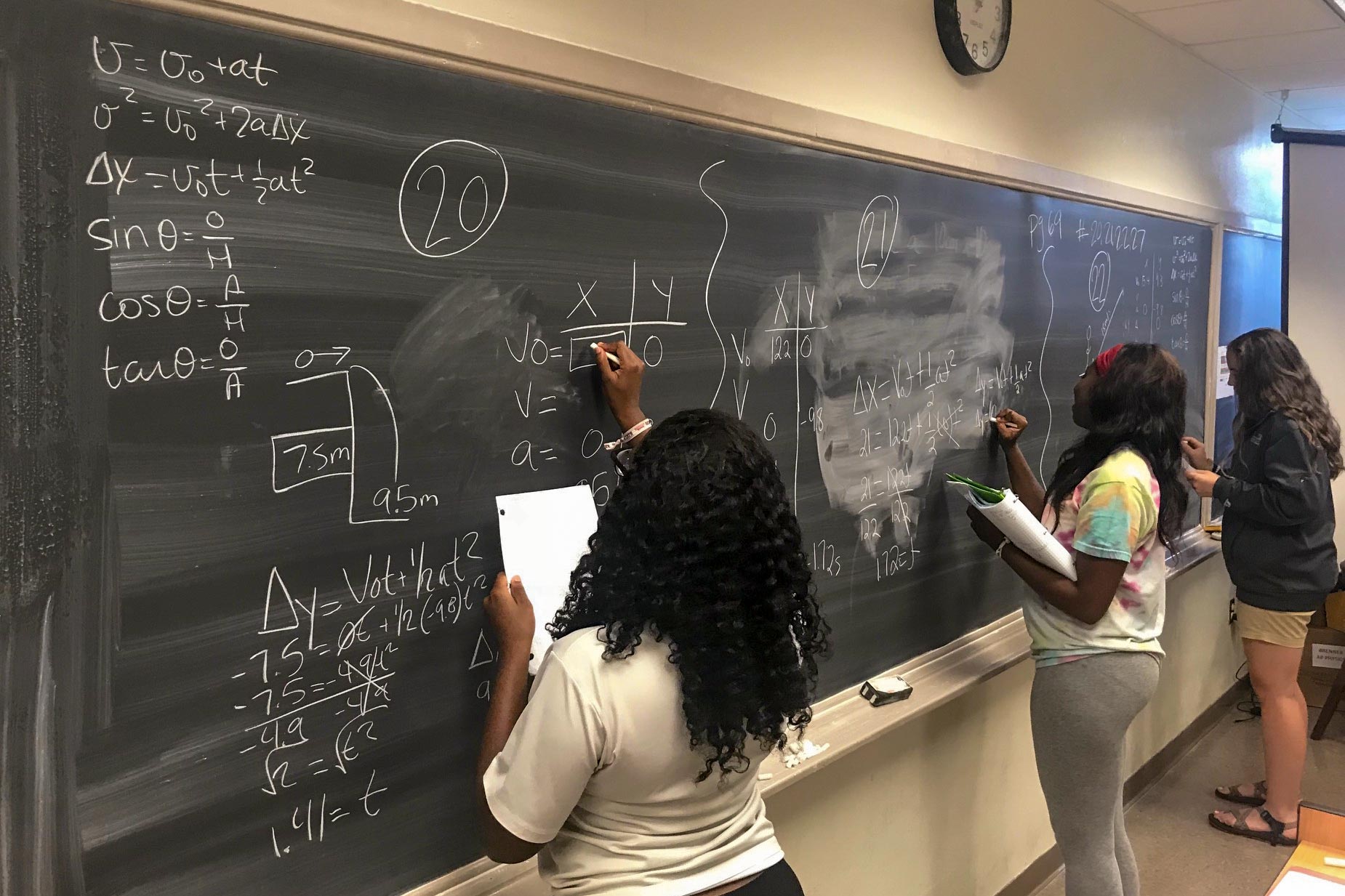 High school juniors work on physics problems on chalkboard