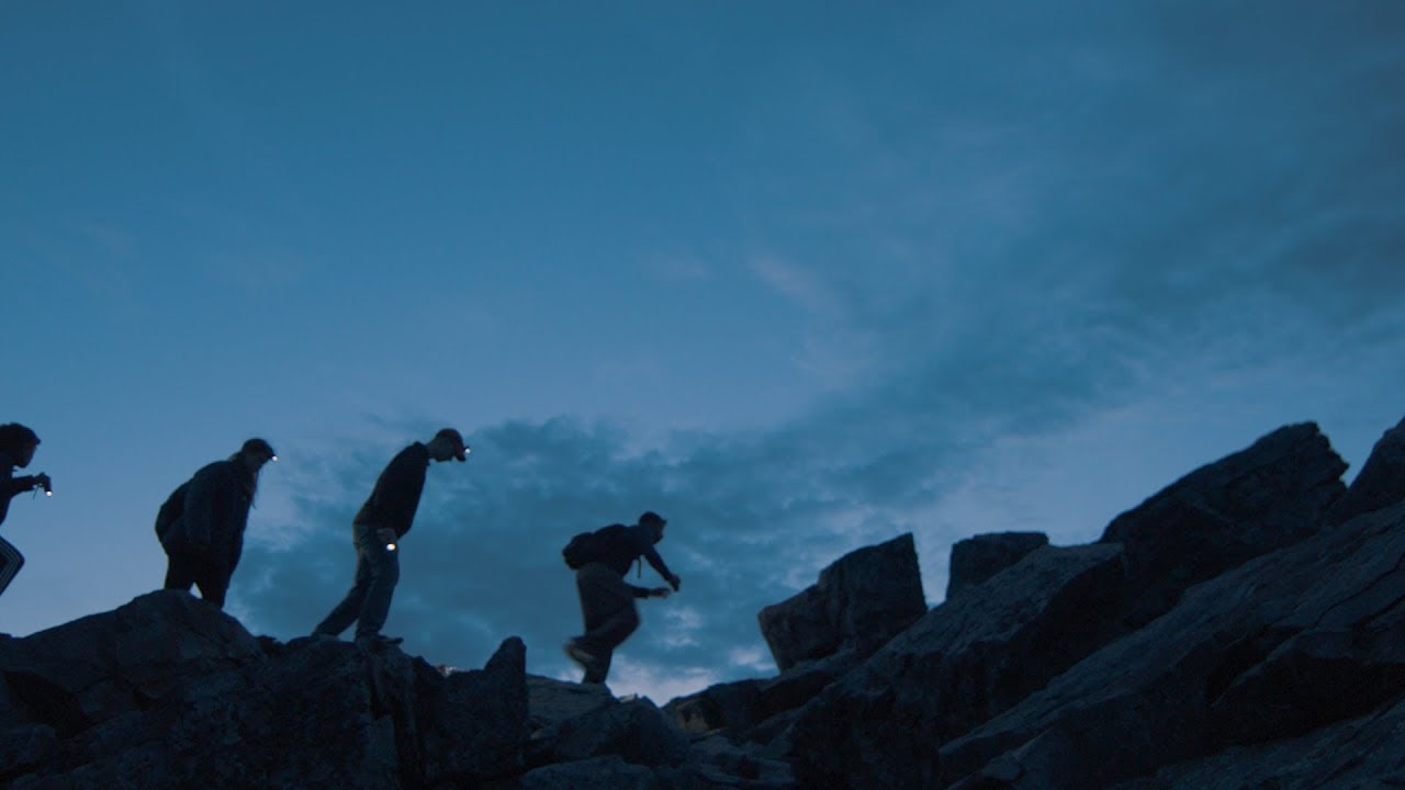Silhouettes of three people hiking on rocks at night