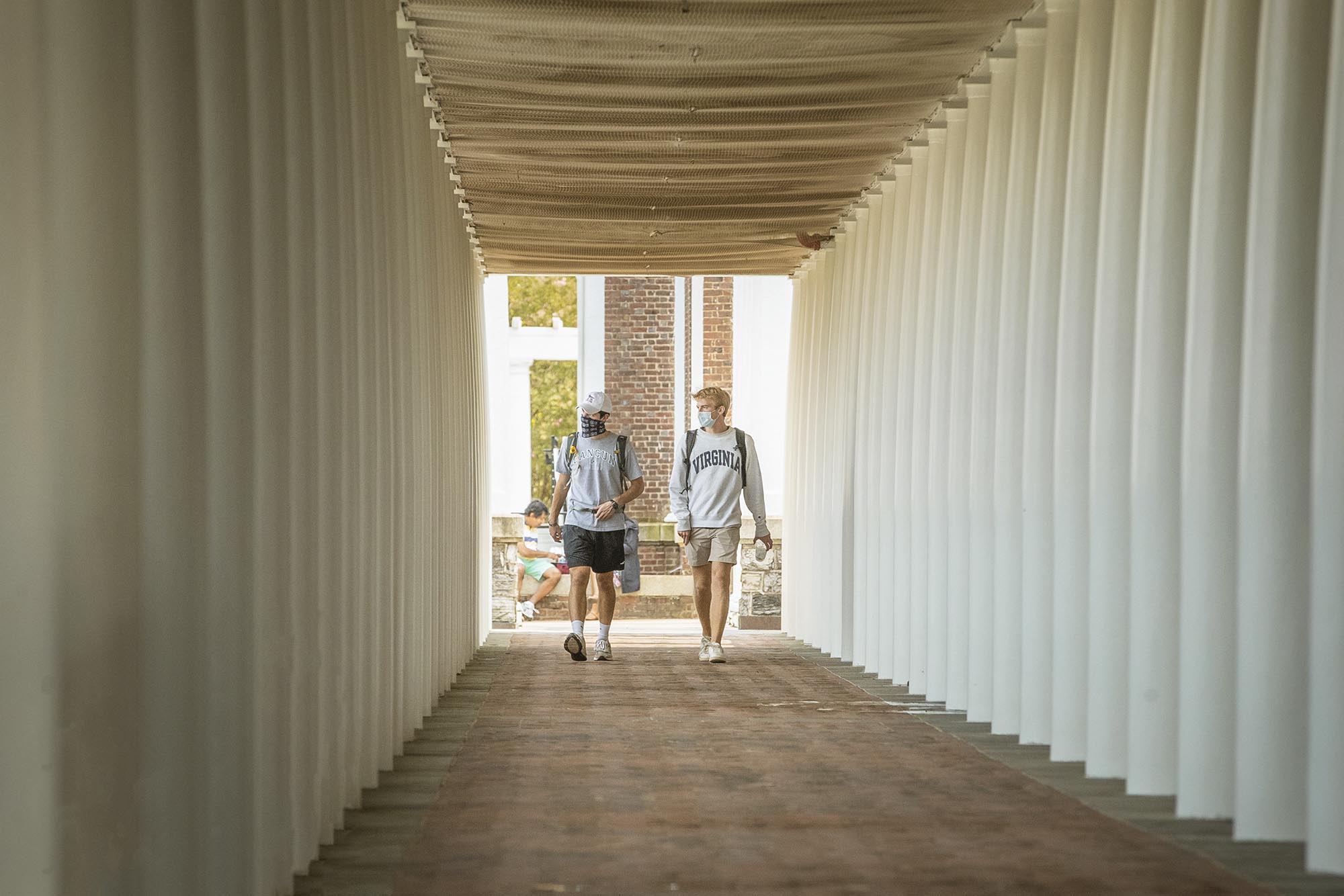Two people walking on a covered walkway lined with tall whit columns
