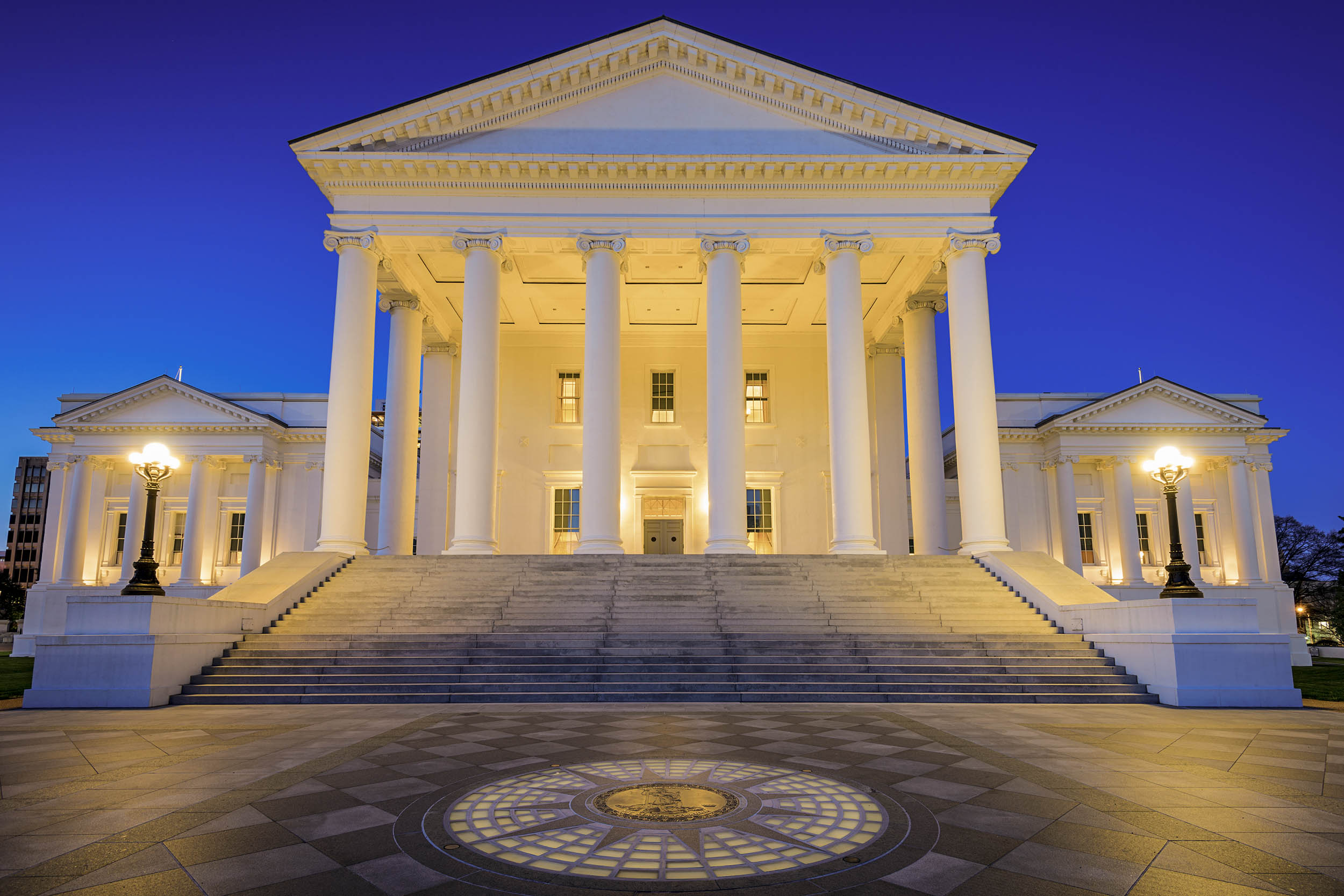 Virginia state Capitol building at dusk.  the white columns and steps are illuminated with yellow lights