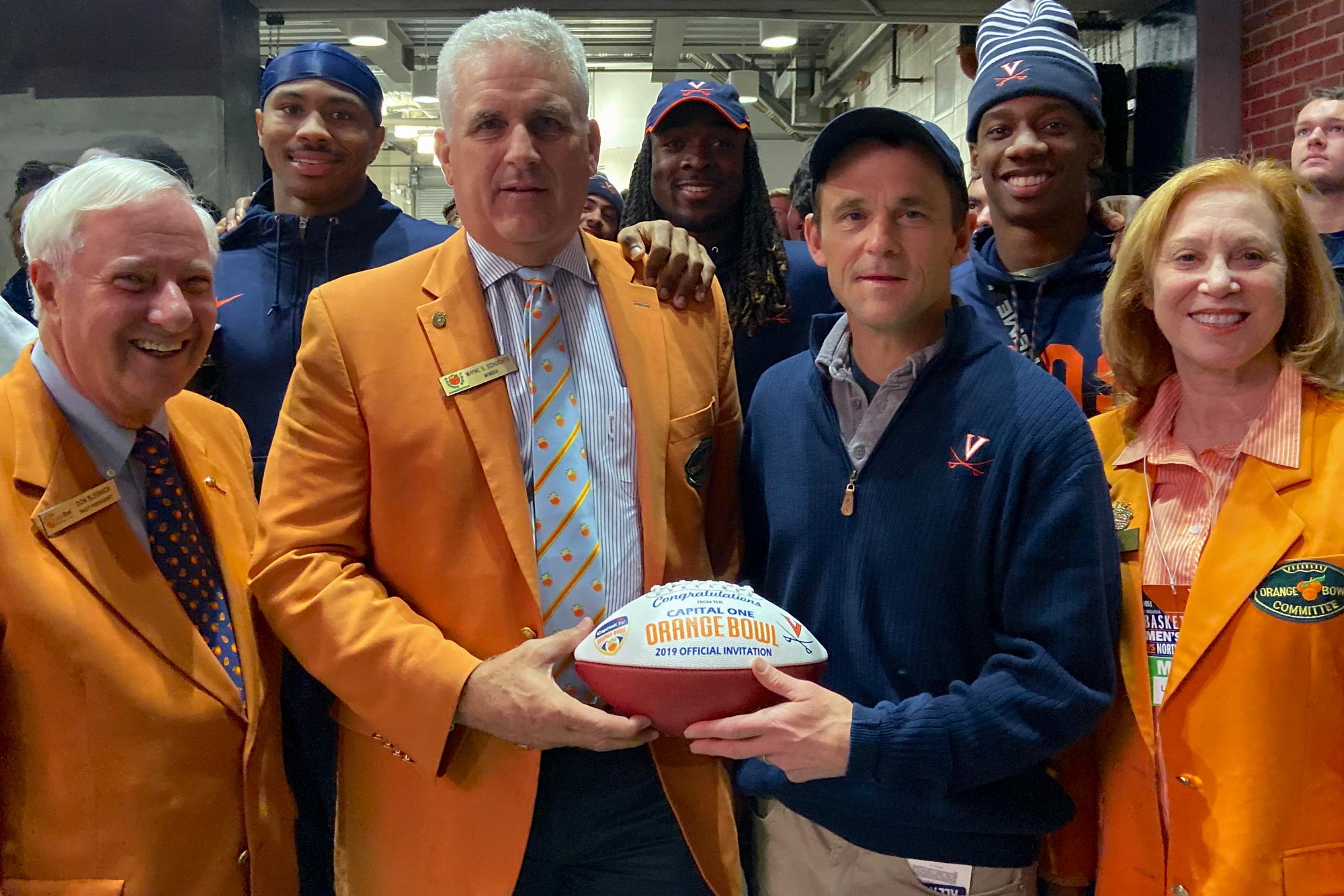 Wayne Schuchts with President Jim Ryan and orange bowl staff and UVA students hold the Orange Bowl football