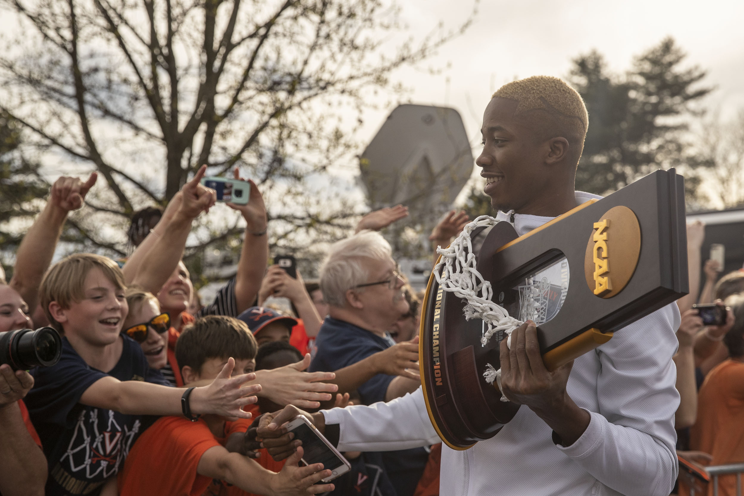 Mamadi Diakite carrying NCAA trophy and basketball net as he high fives the hands of the fans who gathered to welcome the basketball team home