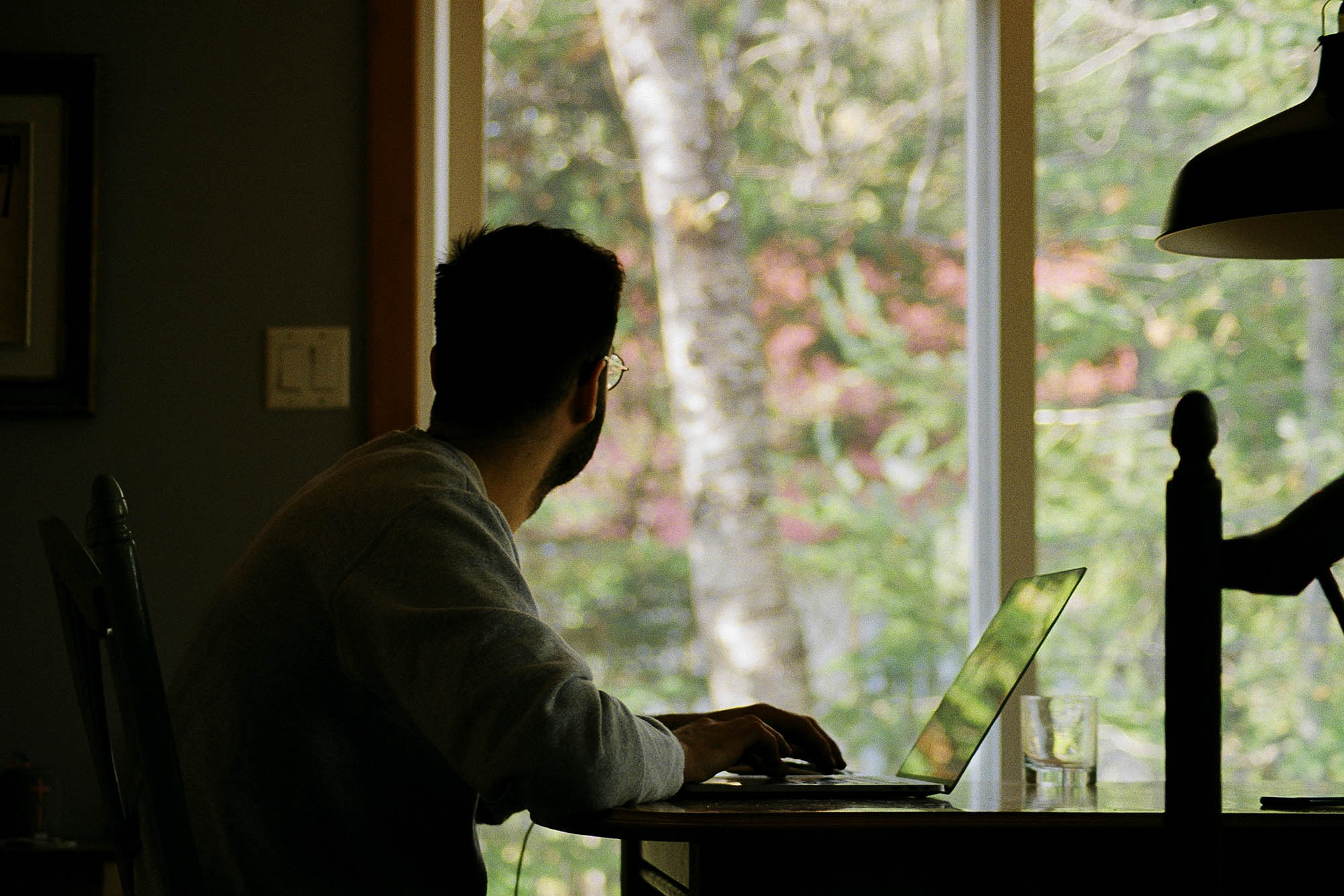Man sitting at a table with laptop looking out their window
