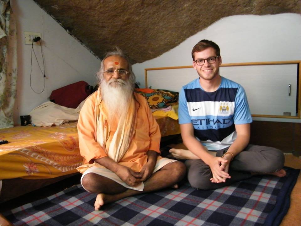 Wade Oakley and Swamiji, sit on the floor with their legs crossed smiling at the camera
