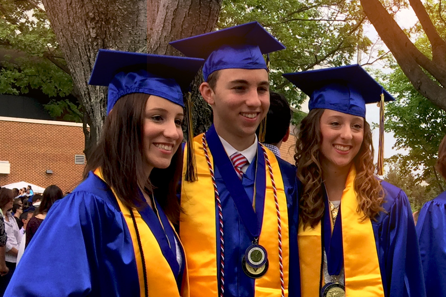 Nina, Noah and Noelle Zorzi stand in their high school cap and gowns smiling for a picture