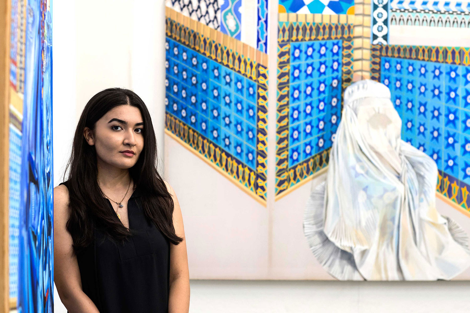 Zuhal Feraidon standing next to a painting looking at the camera