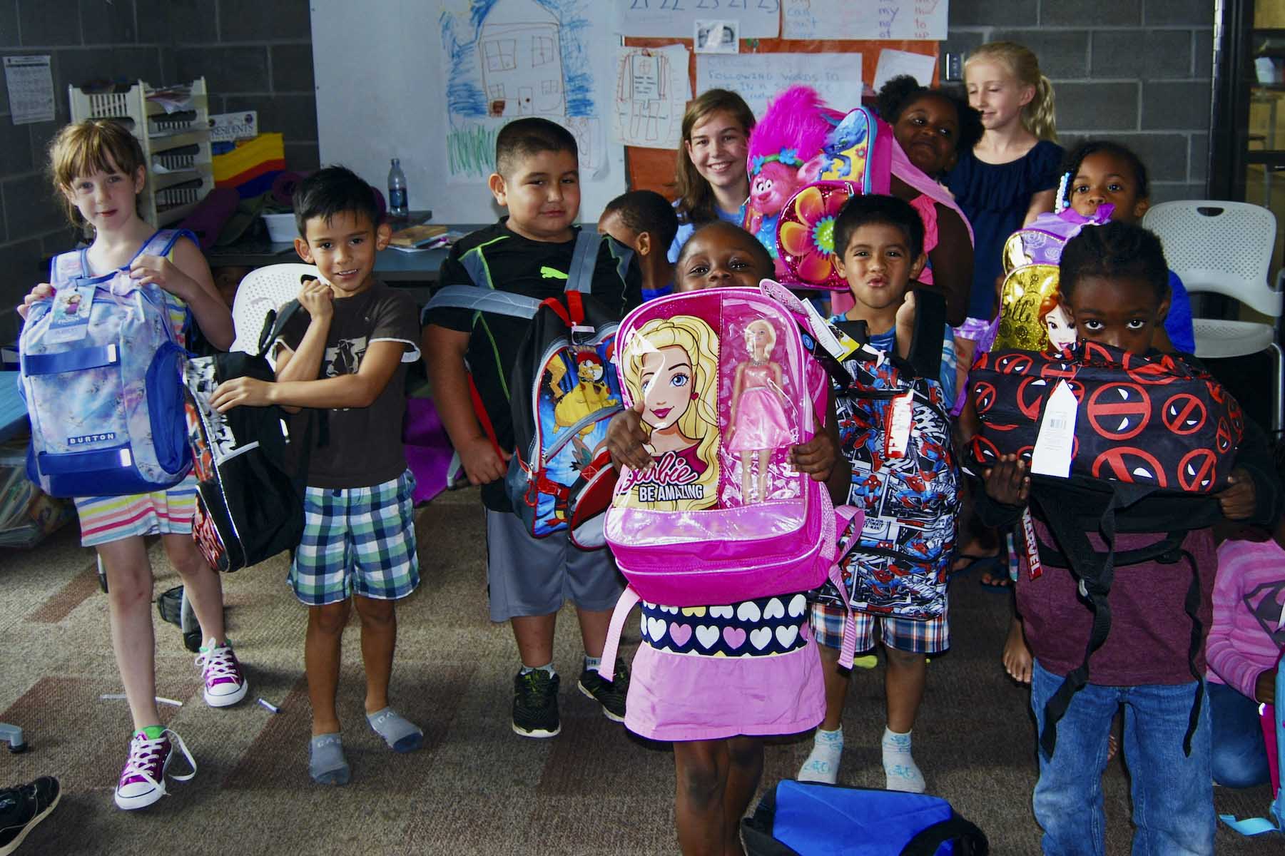 Students gather together for a picture as they hold their new backpacks up to the camera