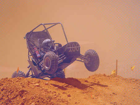 Baja in a go cart over a dirt mound with the front wheels off the ground