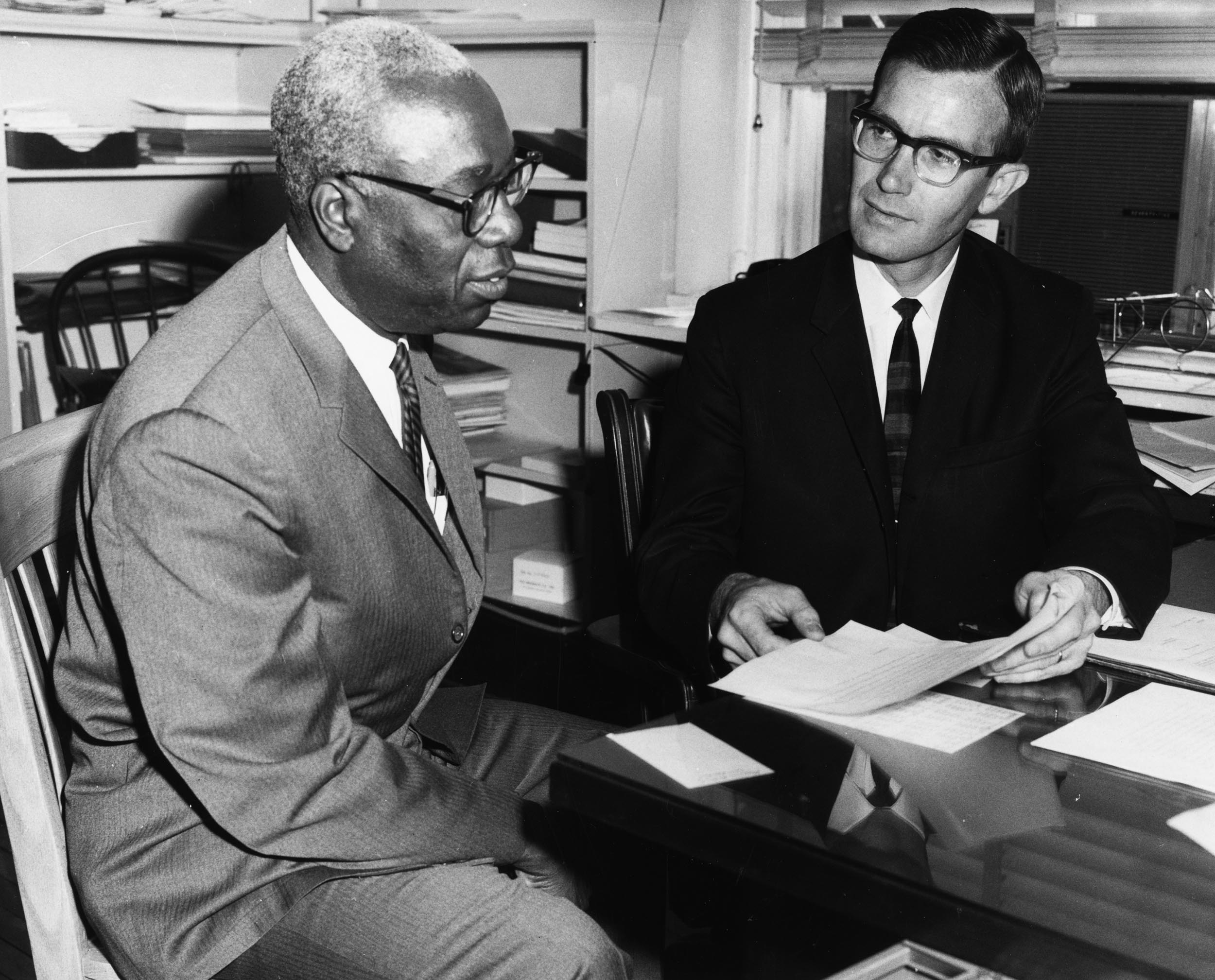 Black and white photo of Two men sitting at a table together looking at a handwritten letter