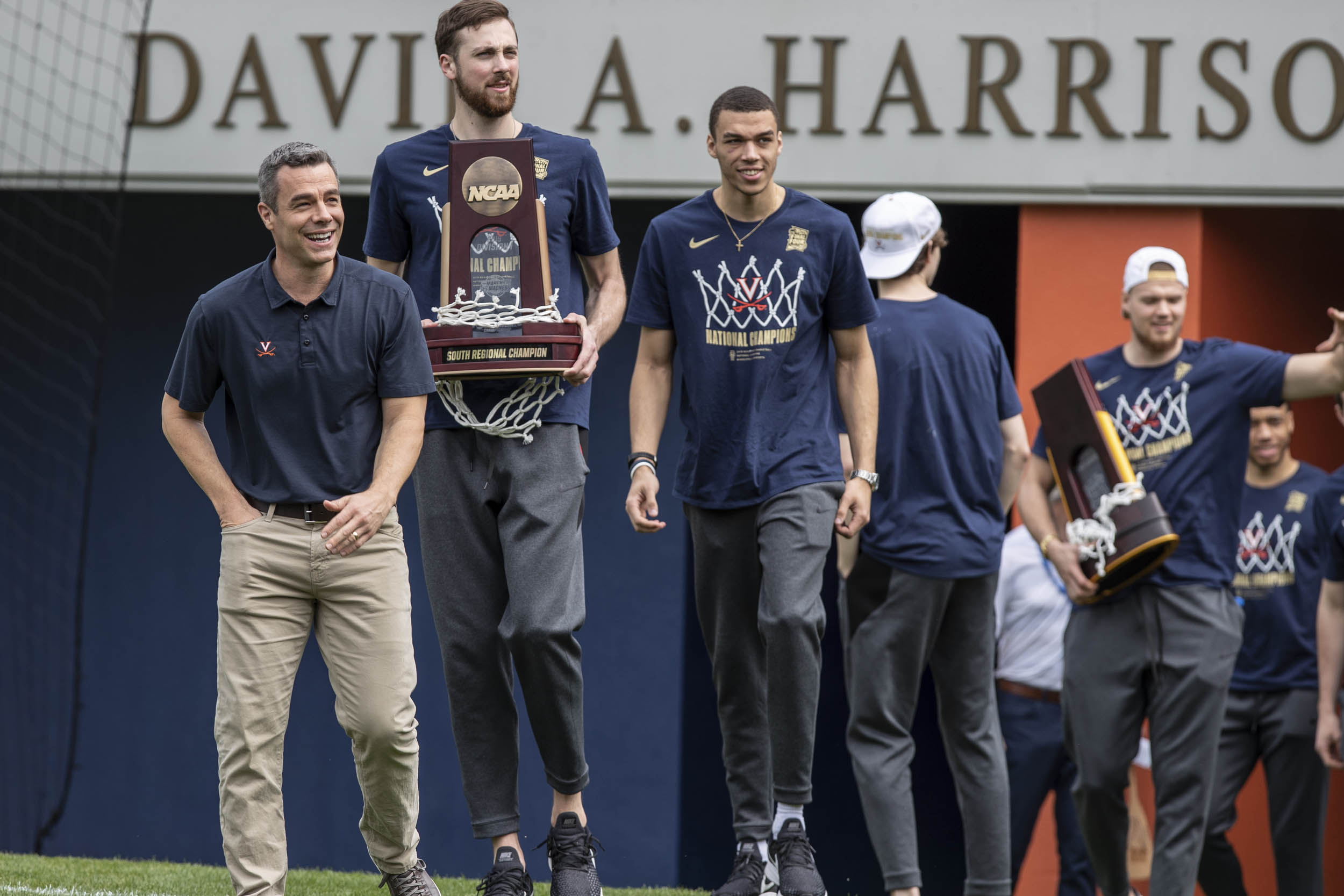 Basketball team walks into Scott stadium carrying their NCAA trophy and winning net