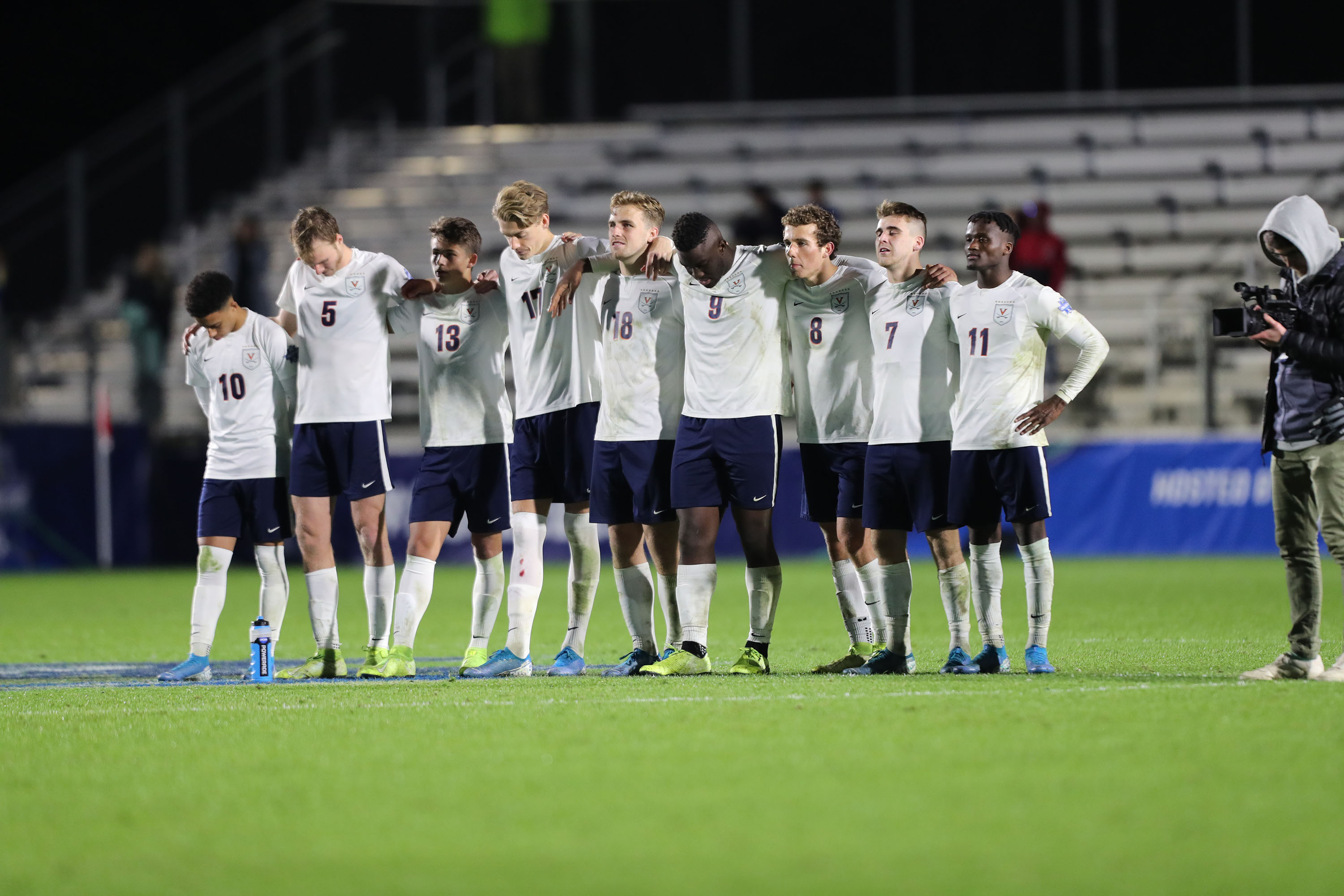 UVA Men's soccer team stand in a line with arms over each others shoulders after a game