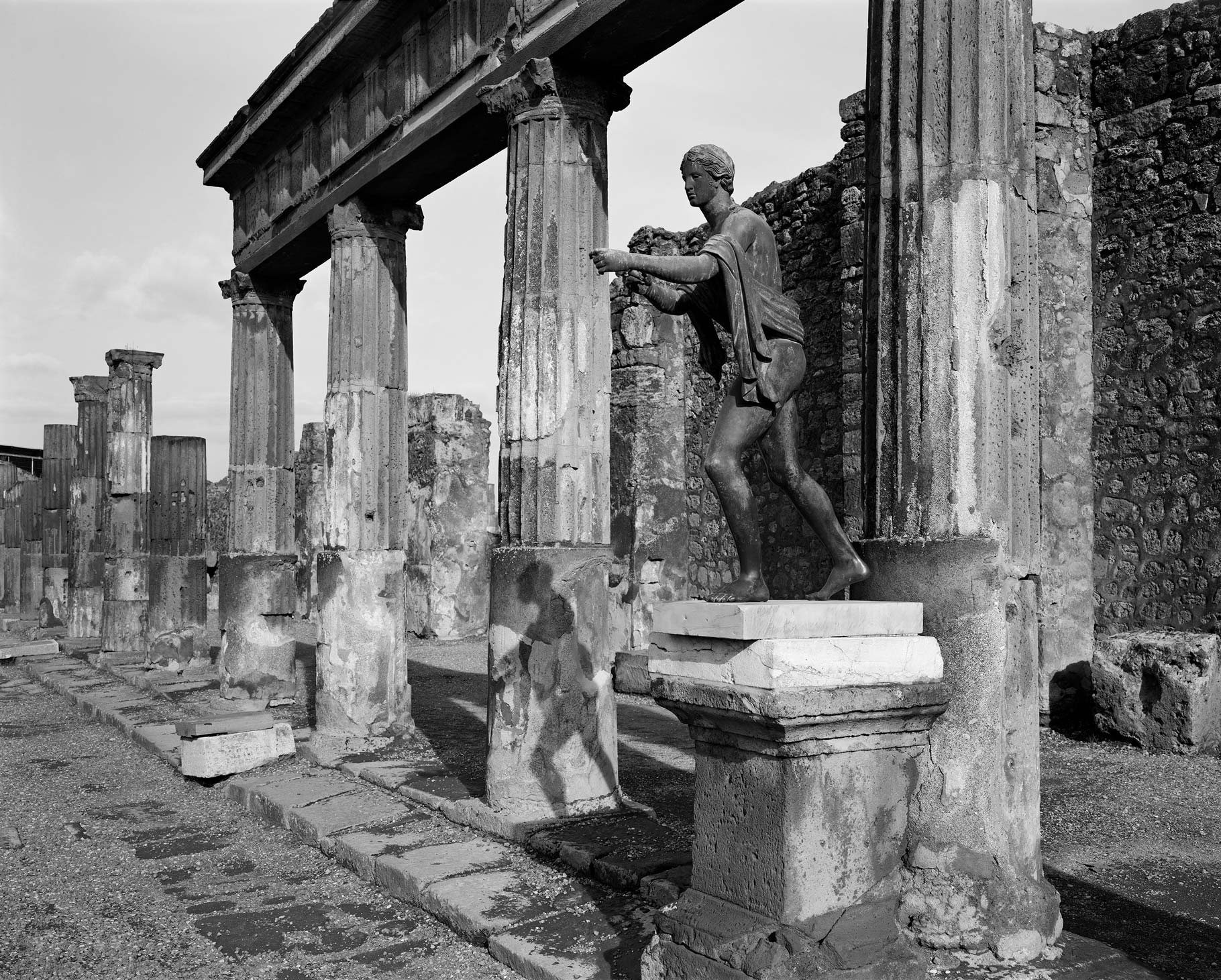 Sculpture on a pedestal outside of a broken building in pompeii, black and white image