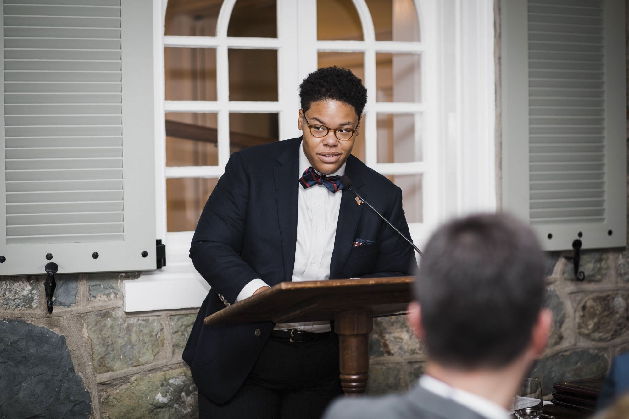 Blake Calhoun dressed in a blue suit and multicolored bow tie speaking at a podium