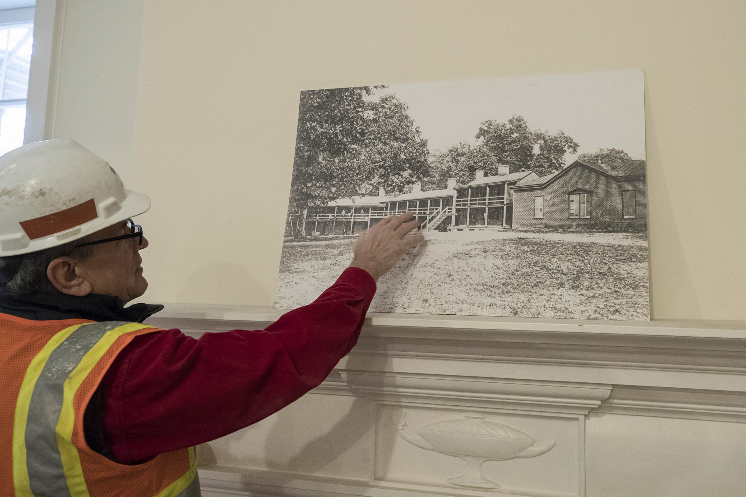 Person in a hardhat pointing to a black and white image on a mantel