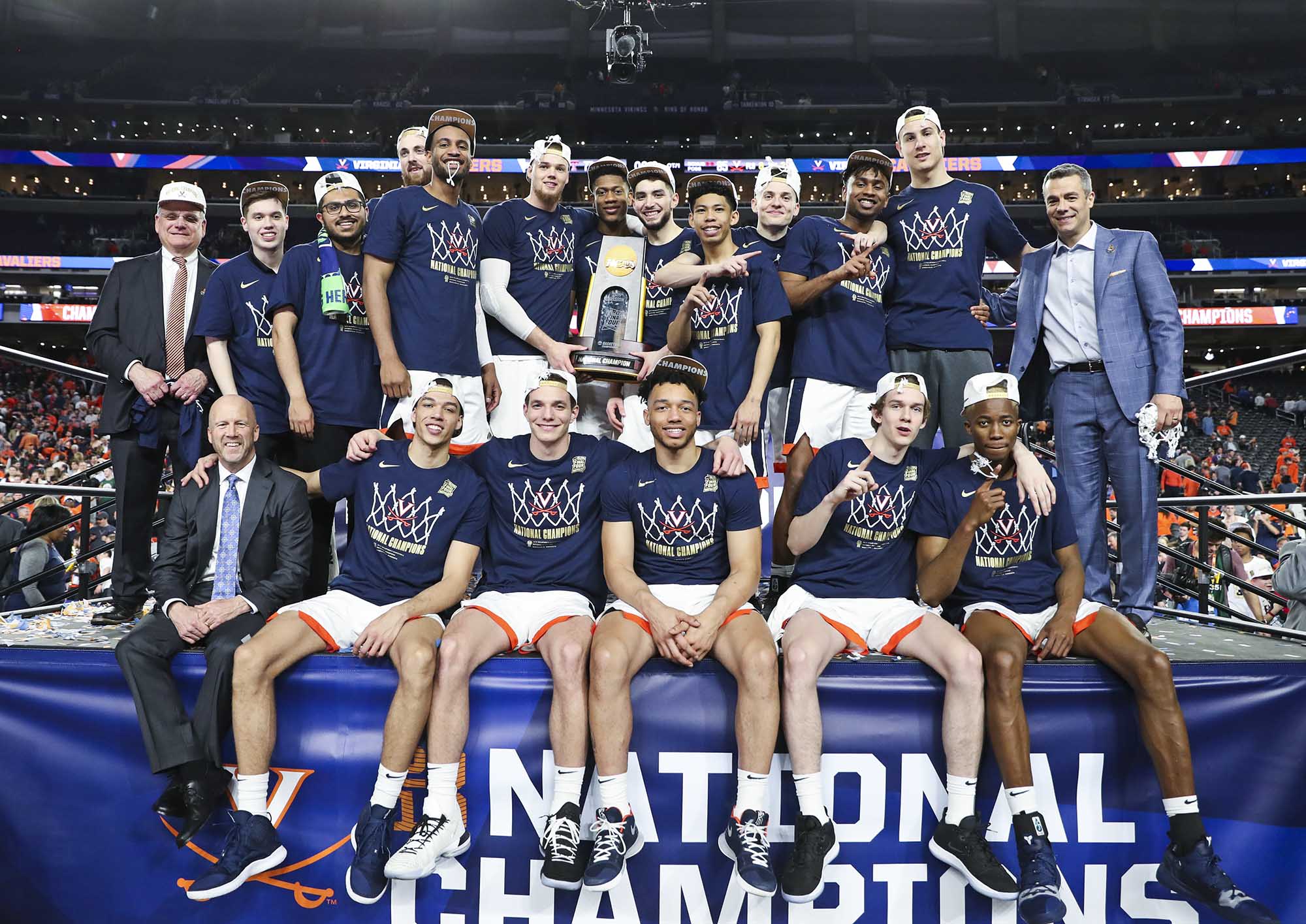 UVA Mens Basketball team sitting on stage holding trophy from their National Championship win
