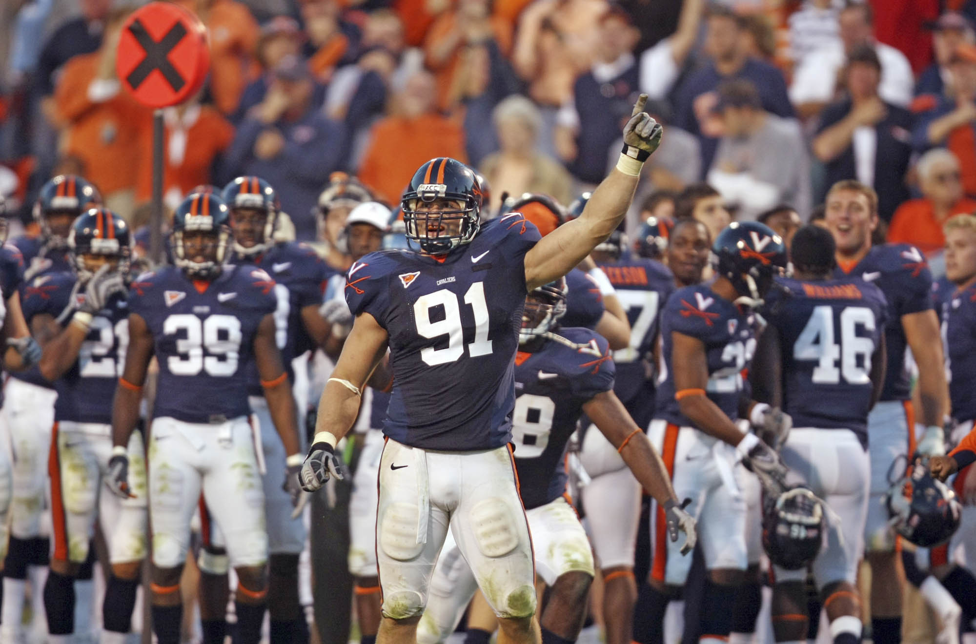 Chris Long in a UVA football uniform during a game Raising his left arm in the air raising his pointer finger to the sky