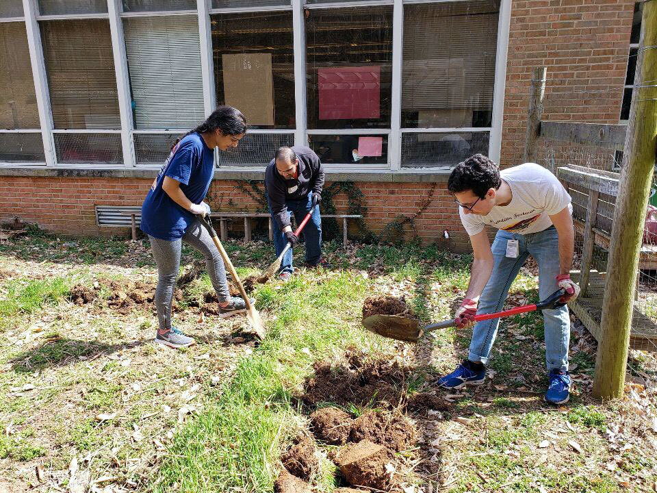 Jasmine Malhi, Naveen Kotha, and Elias Ayoub dig holes in a schoolyard