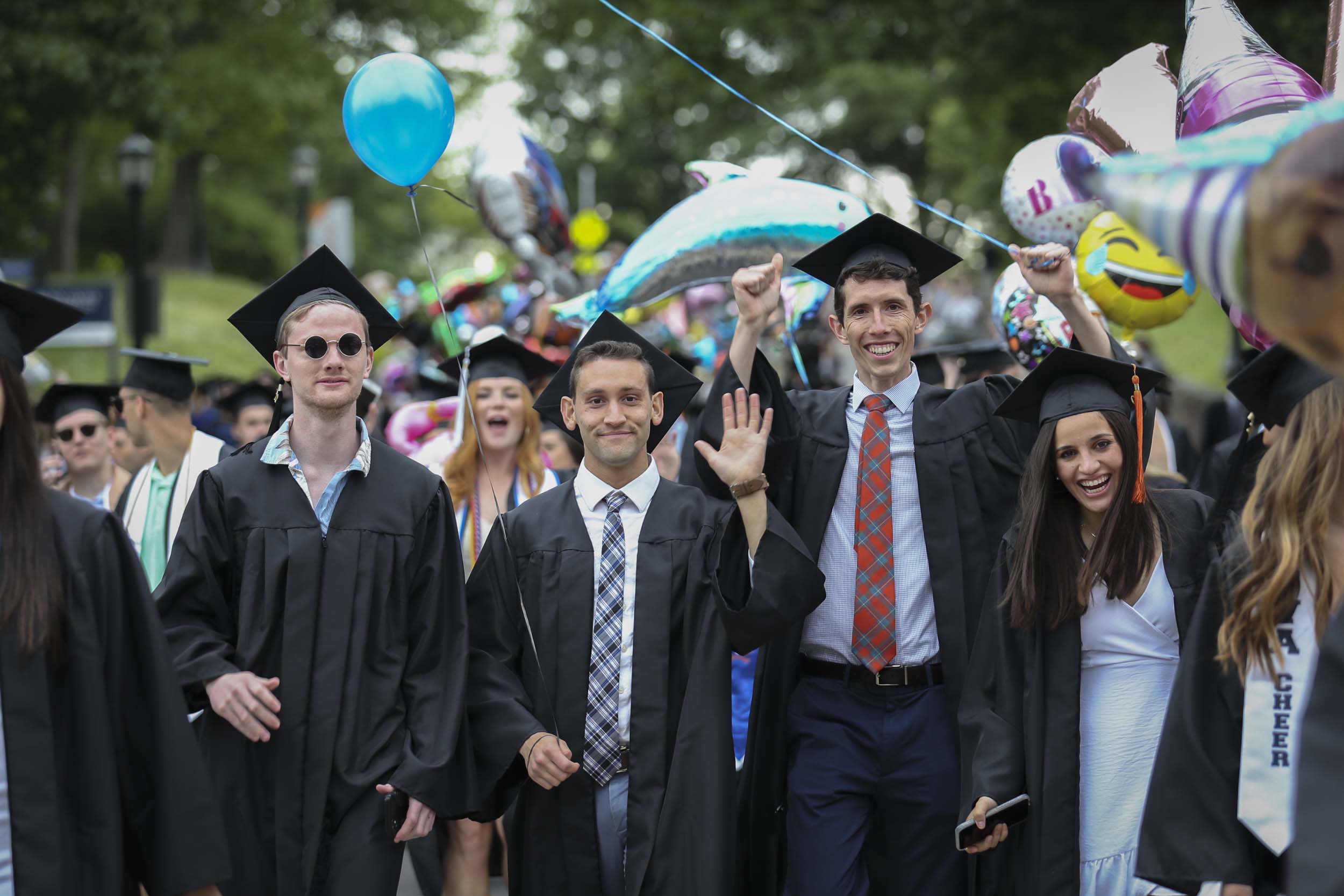 Graduates walking and smiling through Grounds while they carry various balloons