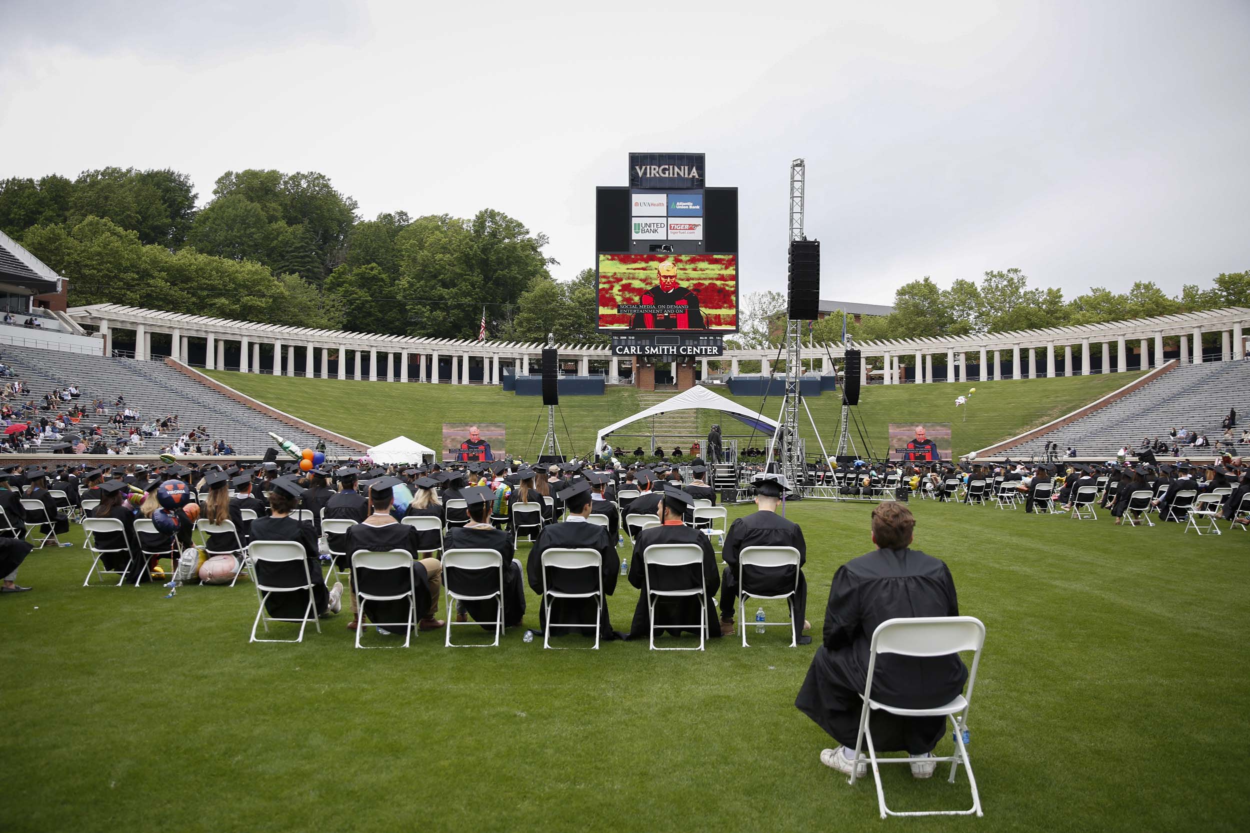 Graduates watching big screen has speaker is shown on the screen