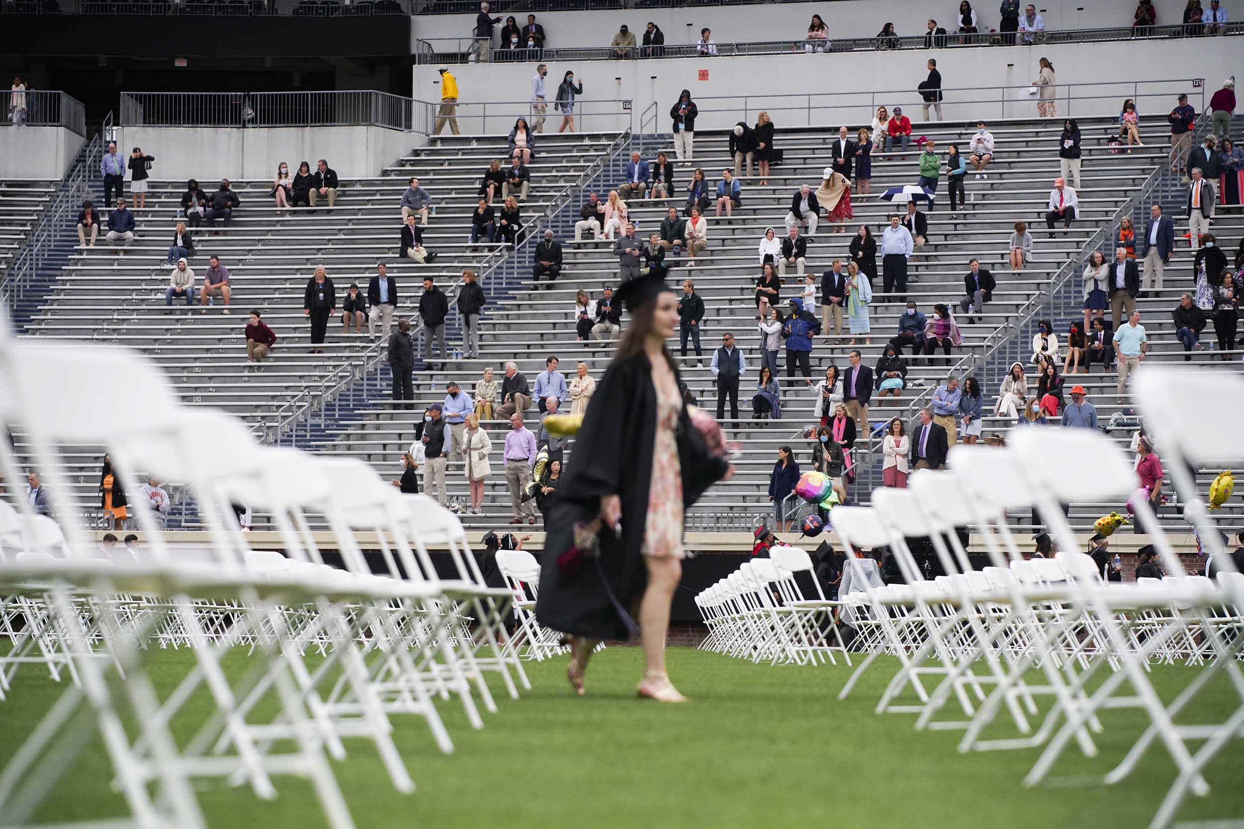 Families gather in the stadium socially distanced as a graduate walks to find a seat