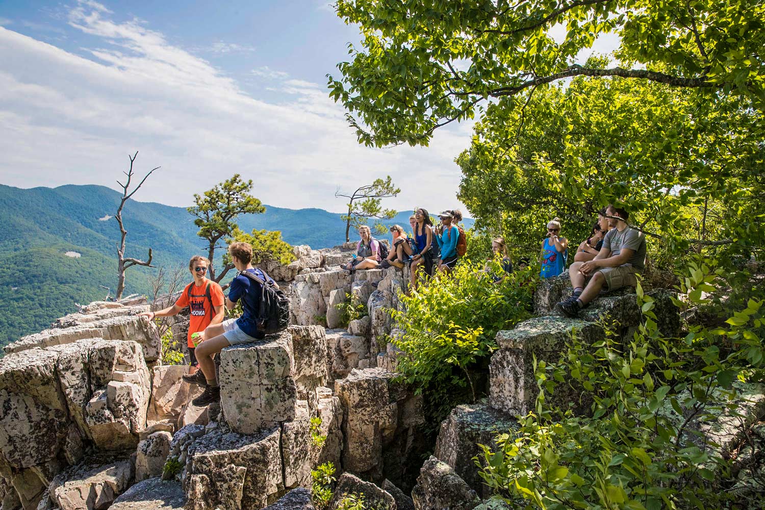 Students sit on boulders talking to each other at the top of a mountain peak