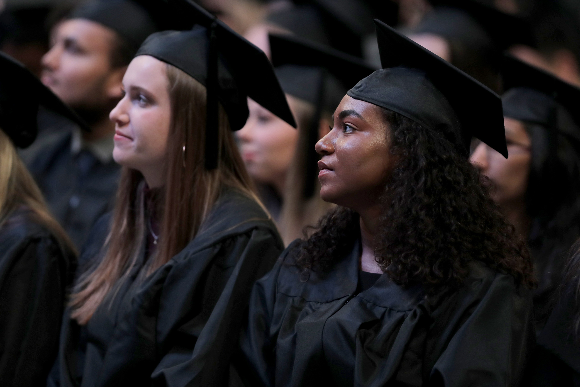 Graduates sit in chairs and watch the stage as a speaker is talking