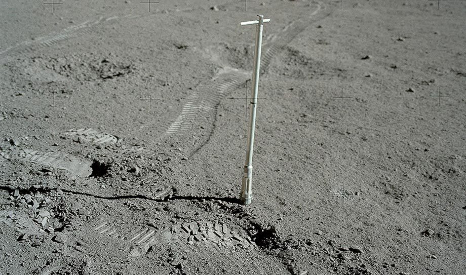 A long white rod is used to extract a core sample from the moon