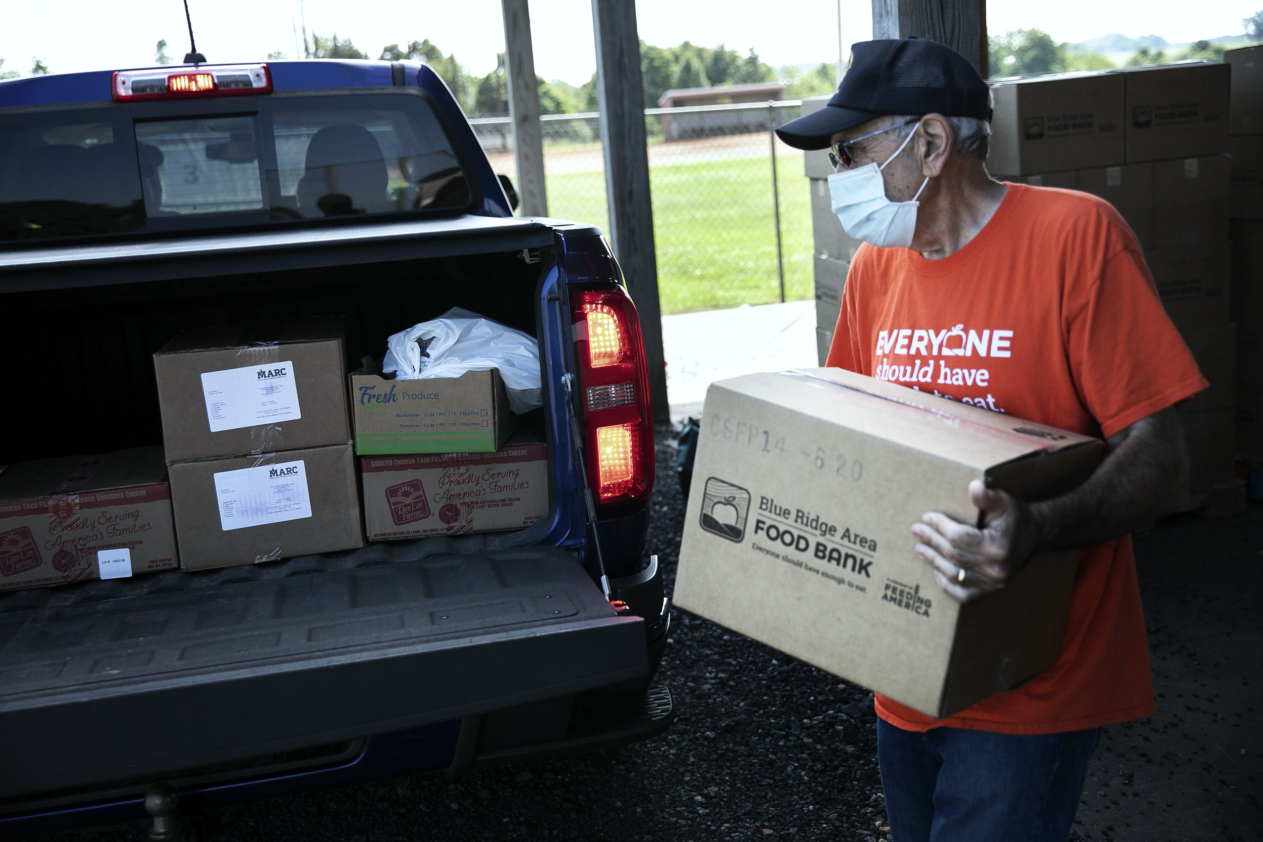 Volunteer in orange shirt loading a Blue Ridge Area Food Bank box into a black truck