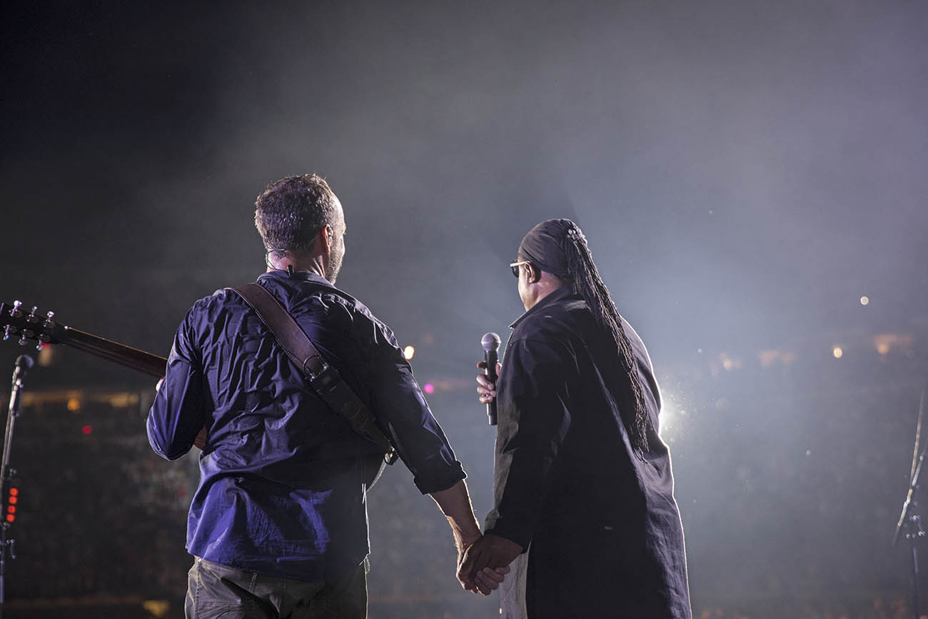 Dave Matthews and Stevie Wonder holding hands in front of a crowded stadium