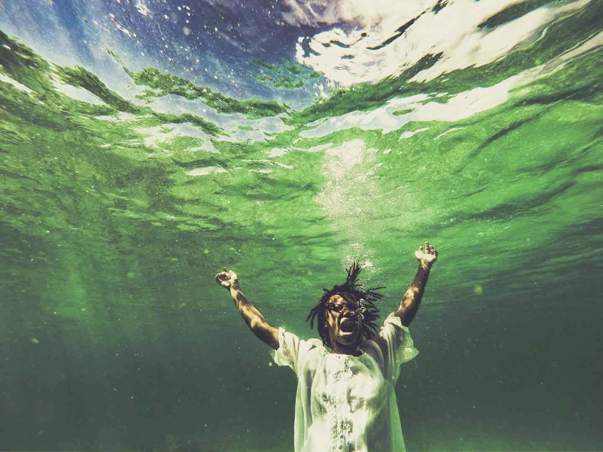 Person under green water with their mouth open