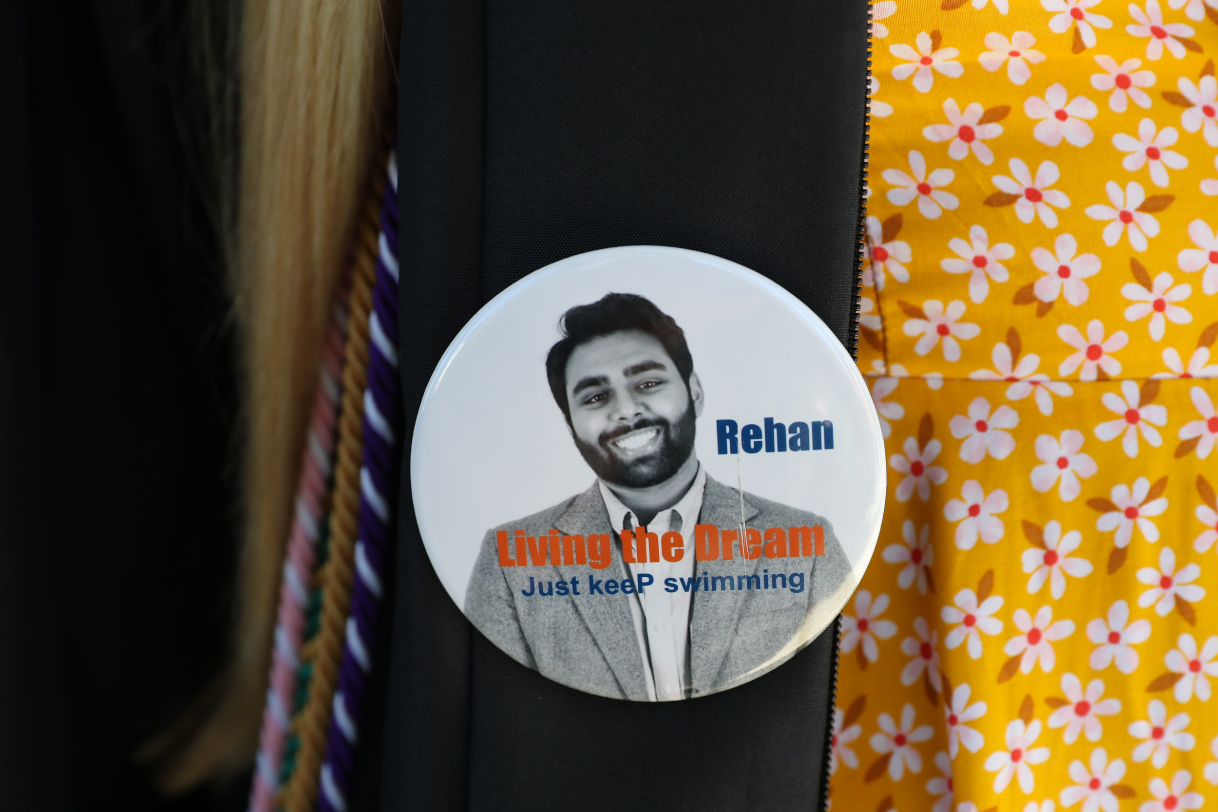 Graduate wears a pin that says Rehan Living the Dream Just keeP swimming