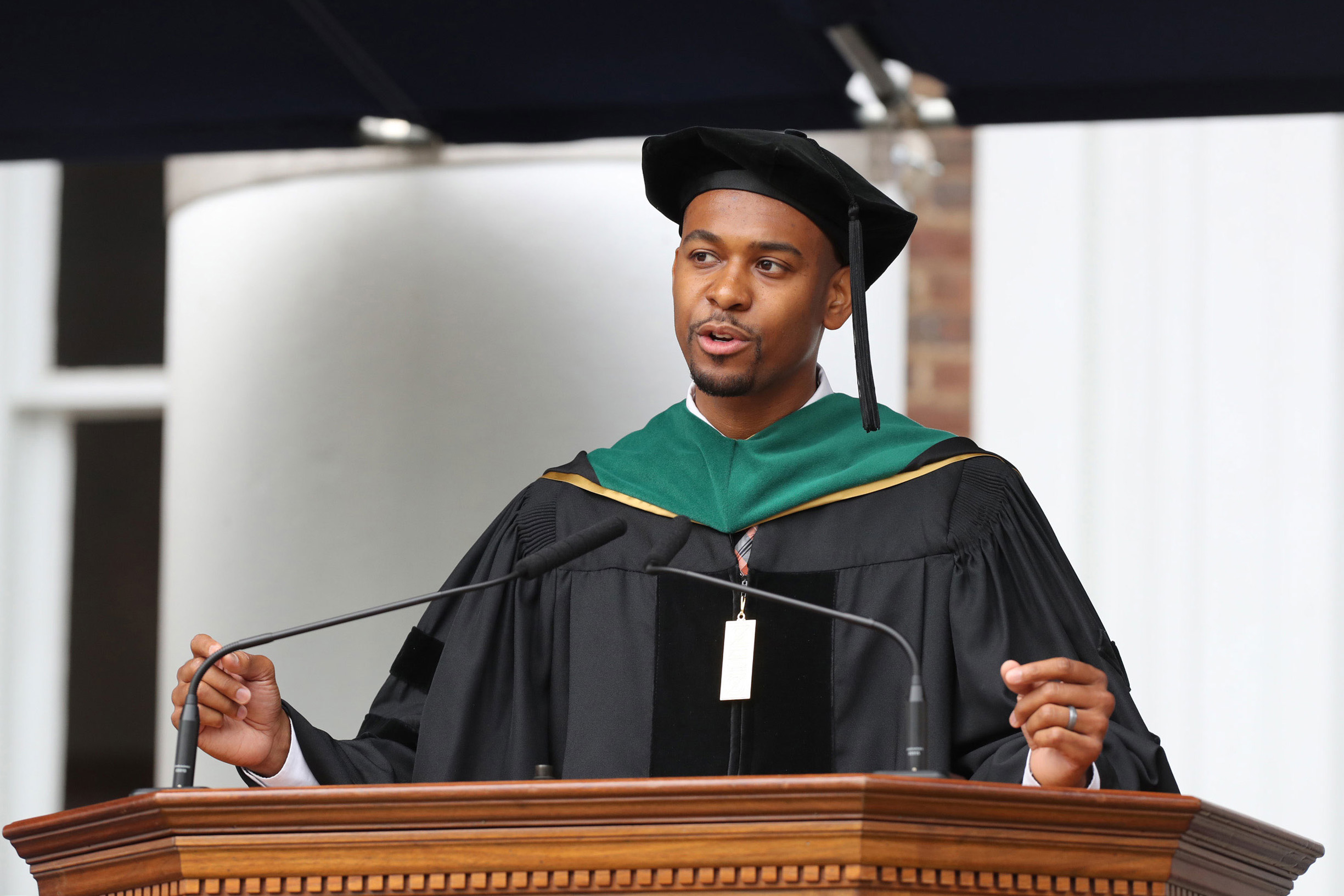 Cameron Webb stands at the podium giving a graduation speech in his doctorate cap and gown