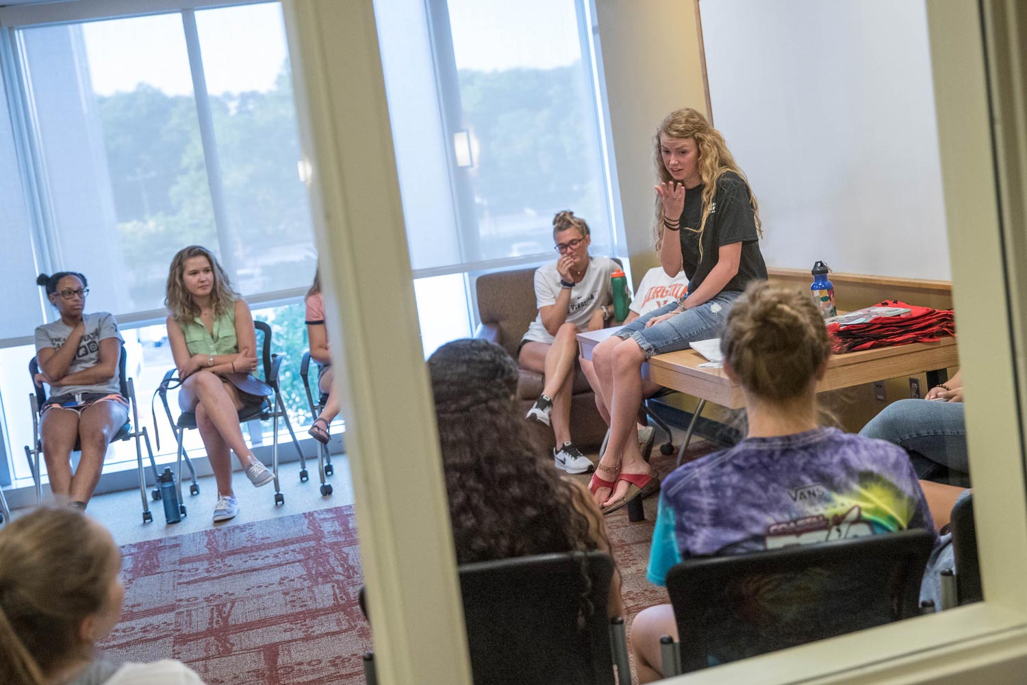 Rebecca Lewis sits on a table and talks to fellow students  who are sitting in chairs in a circle