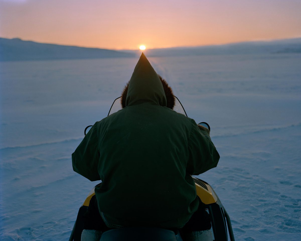 An Inuit man driving a snow mobile at night