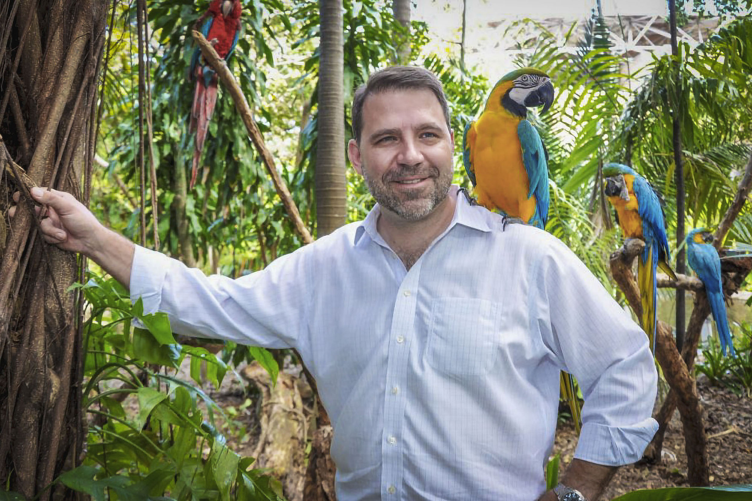 Dunlap standing next to a tree with parrot on his shoulder and parrots around him