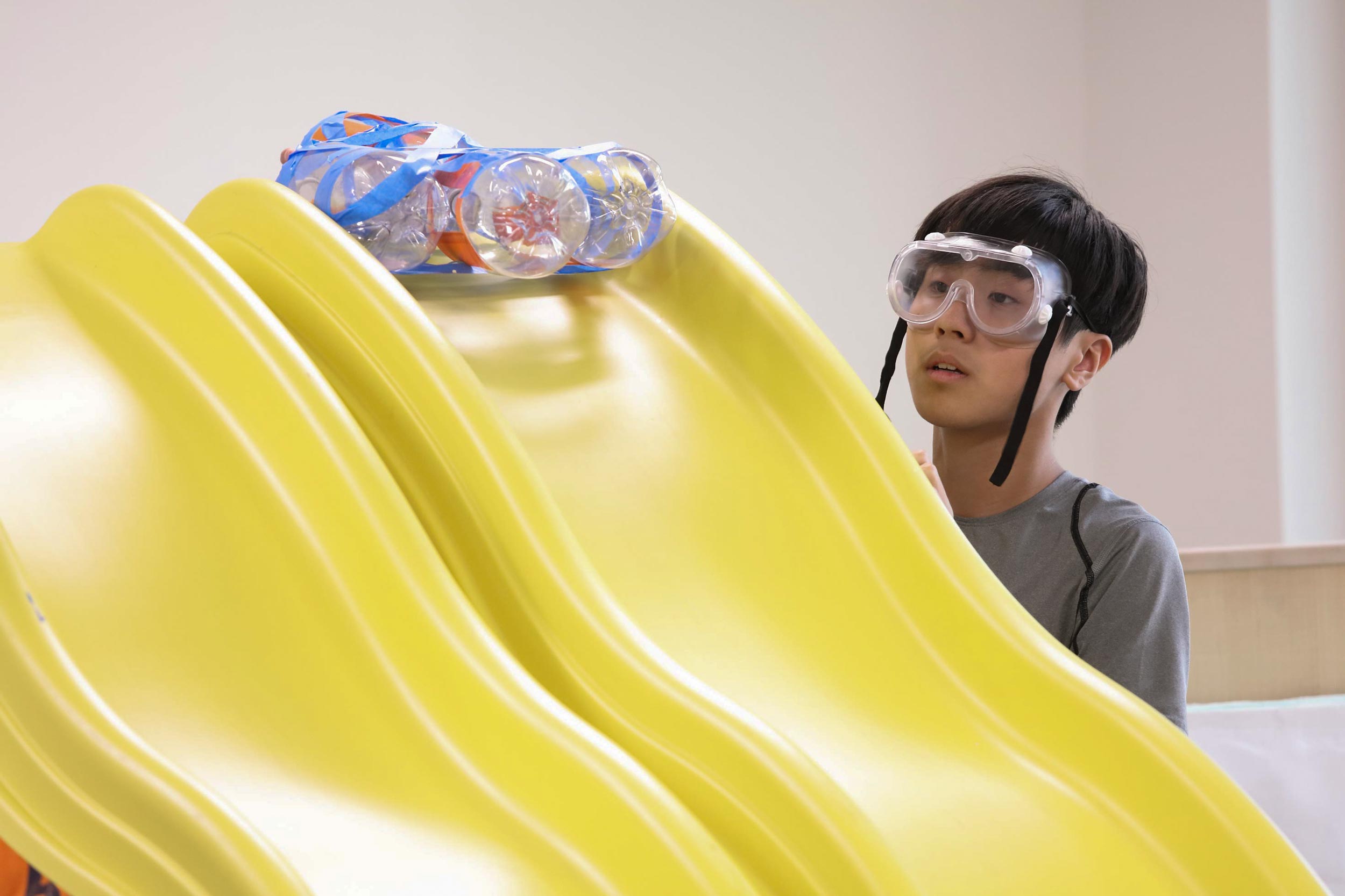 An engineer student through his safety goggles at his team’s vehicle at the top of a yellow plastic slide
