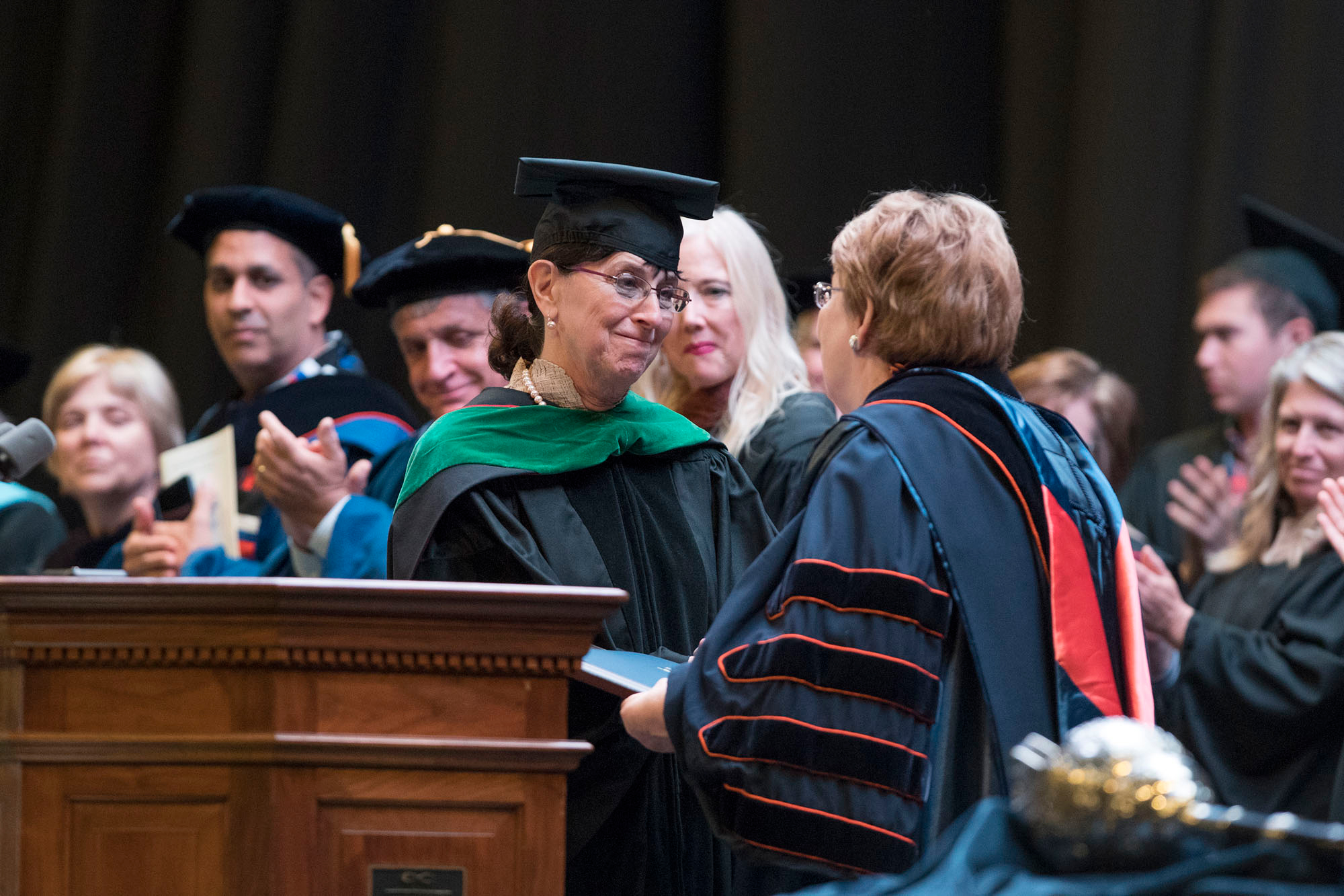 Dr. Karen S. Rheuban,  shakes President Teresa A. Sullivan hand on stage