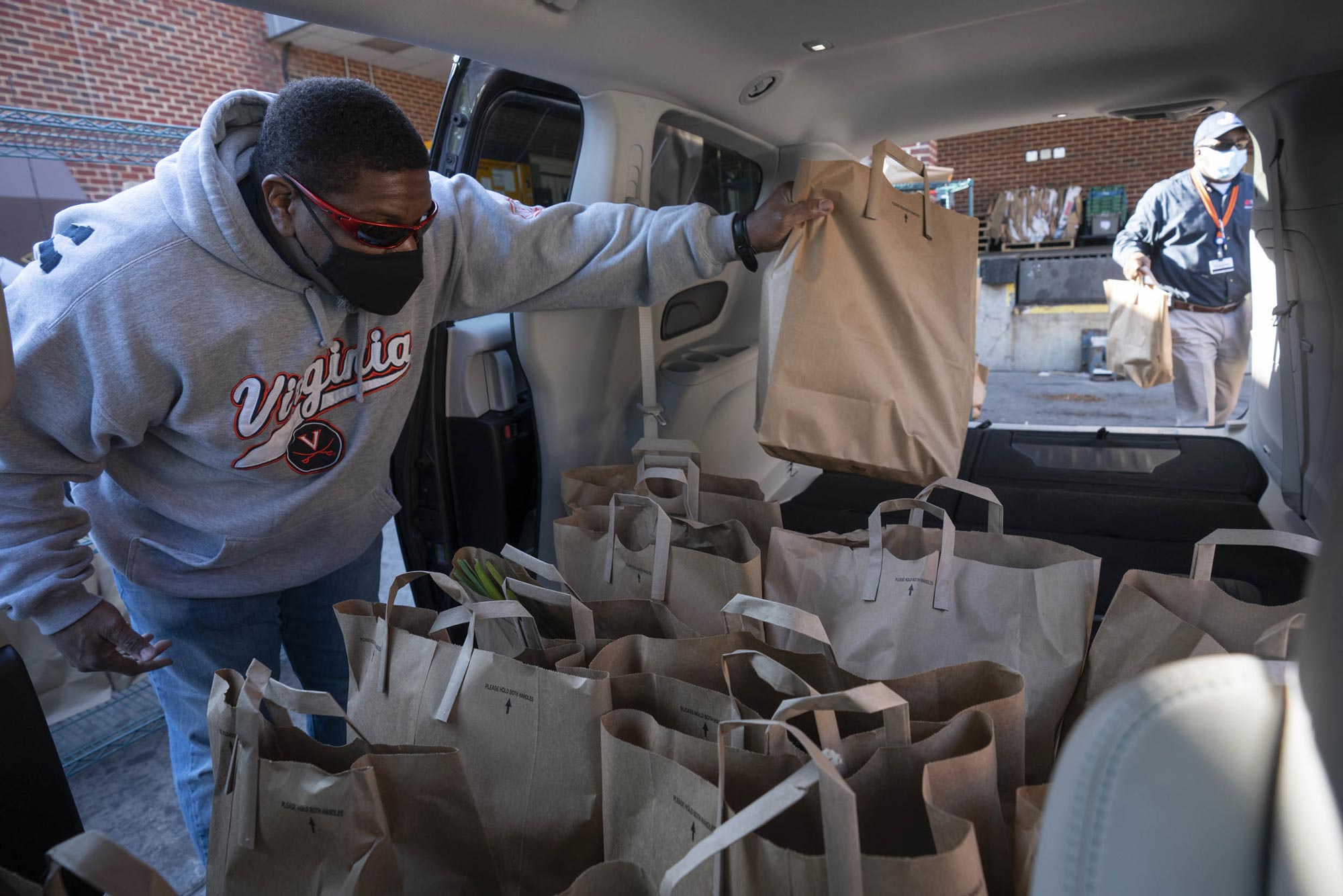 Man placing a brown bag of food in the back of a van to be delivered to those in need