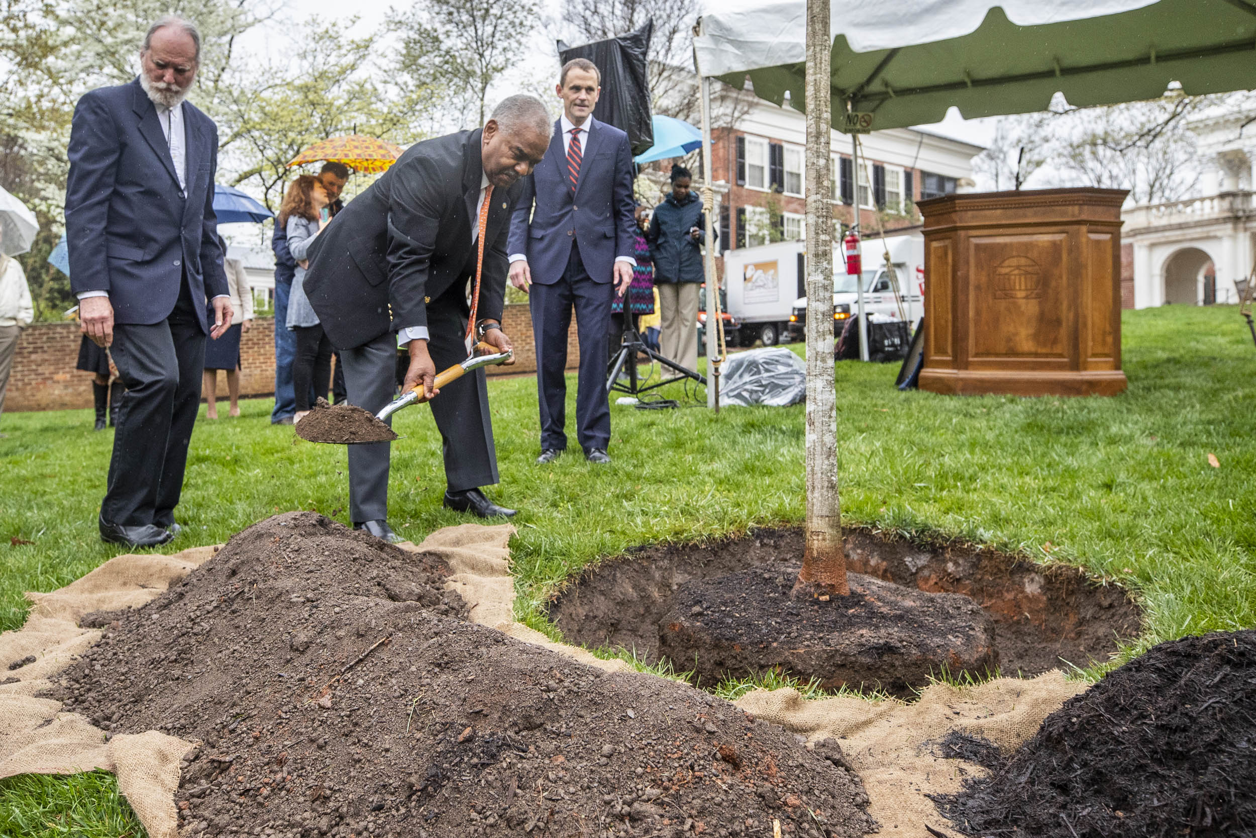 Man places dirt over a tree at a tree planting ceremony